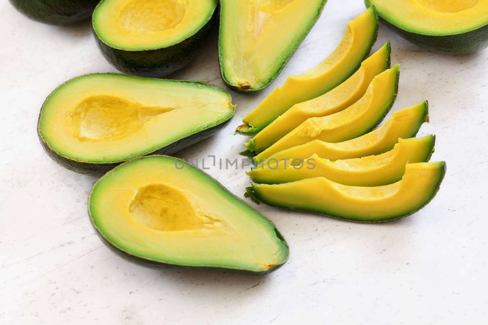 Avocado pieces and halves with bright yellow fruit pulp on white stone board by Ivanko