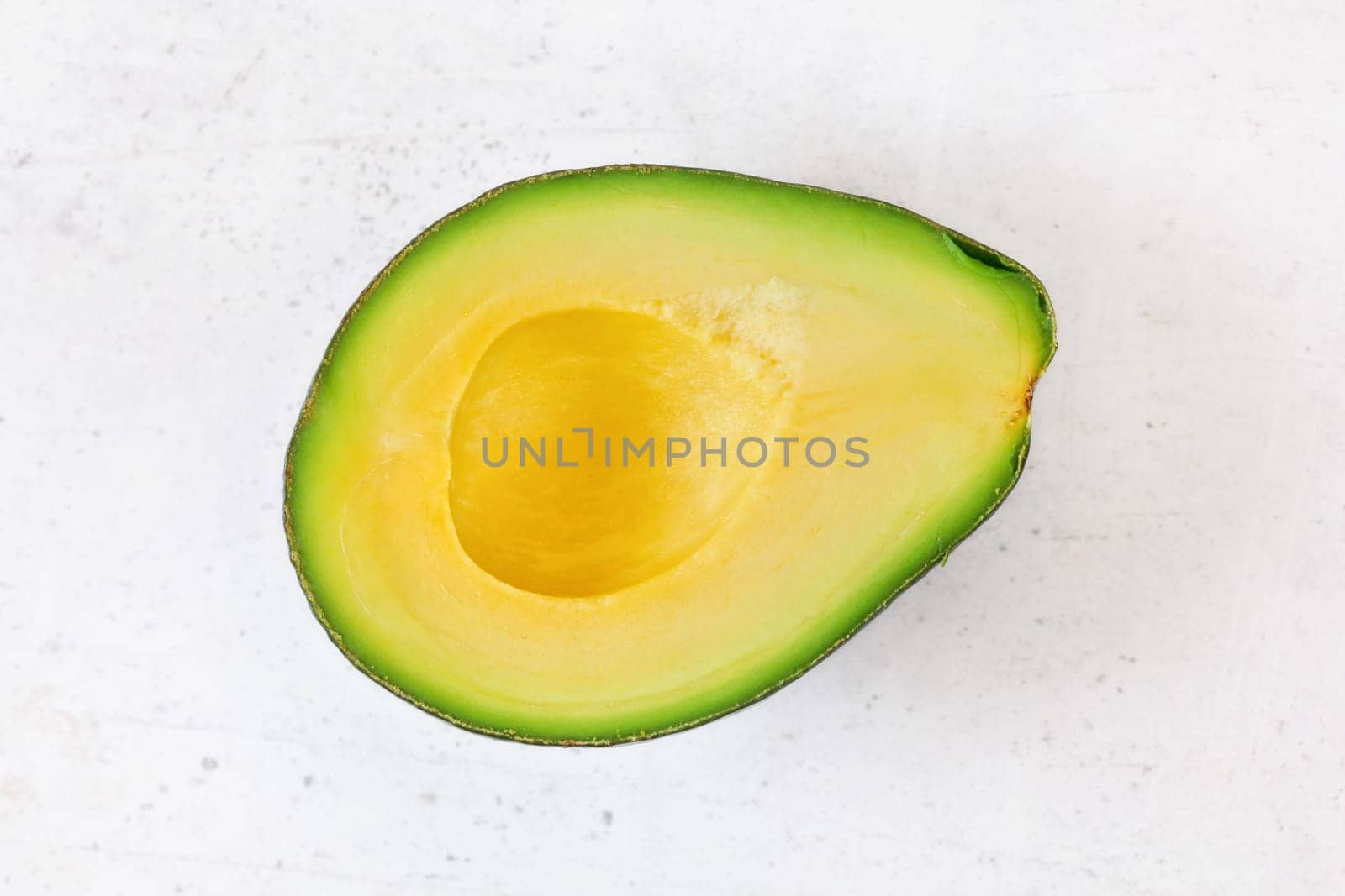Top down view, halved avocado with yellow fruit pulp on white stone board