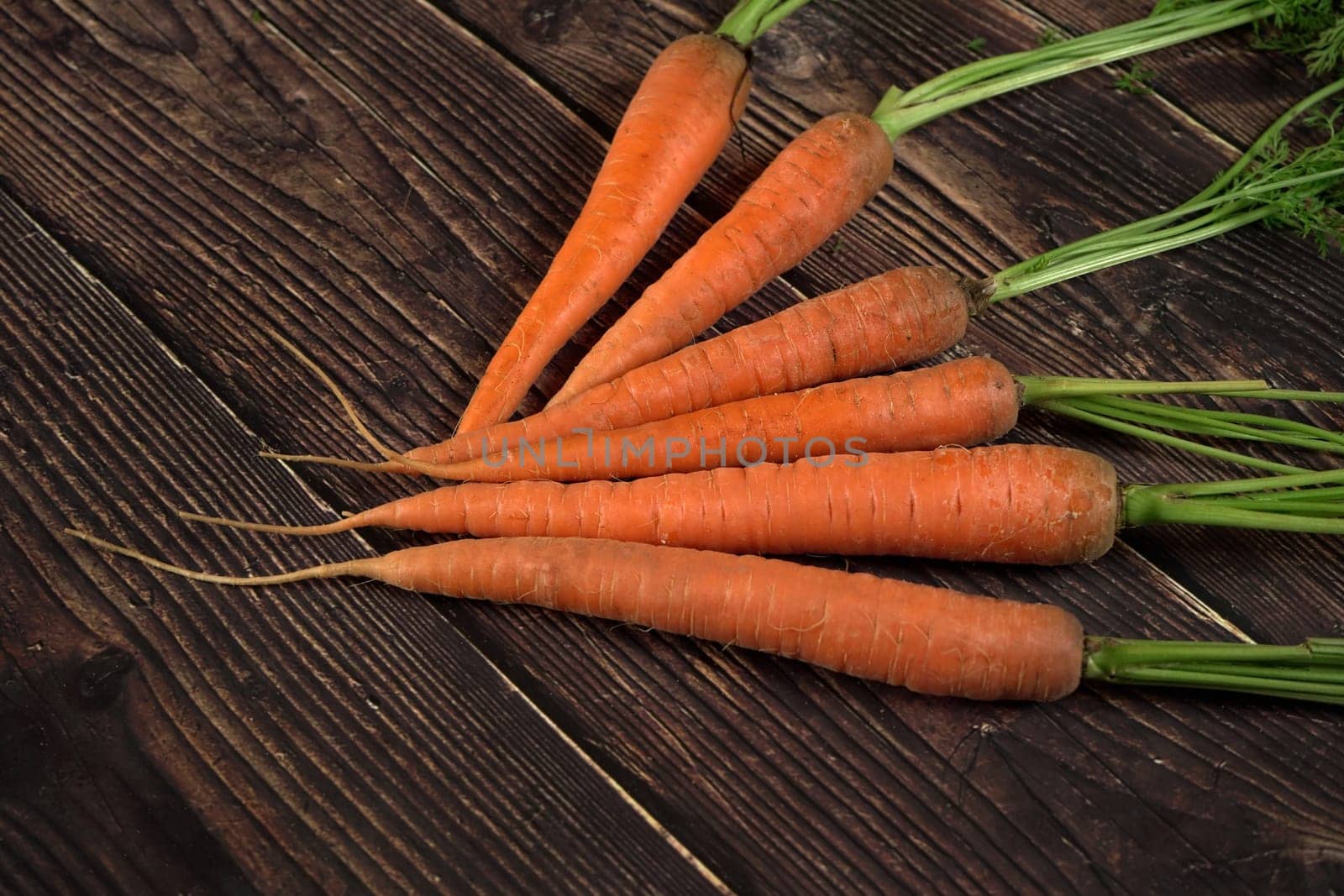 Fresh organic carrot roots on dark wooden board by Ivanko