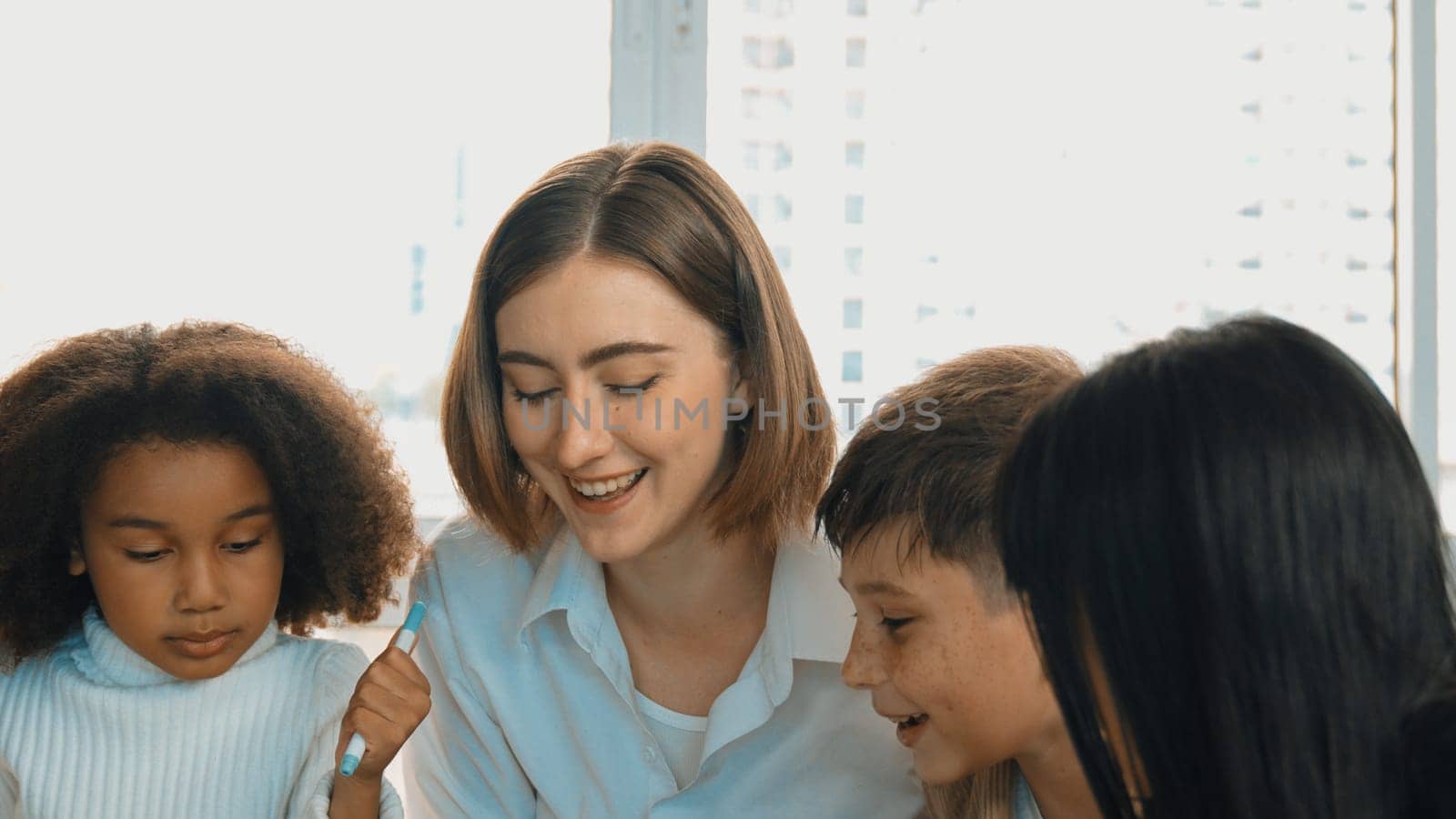 Happy diverse student and smart teacher drawing and coloring by using marker at drawing book. Multicultural smart learner using drawing book while talking to skilled caucasian instructor. Erudition.