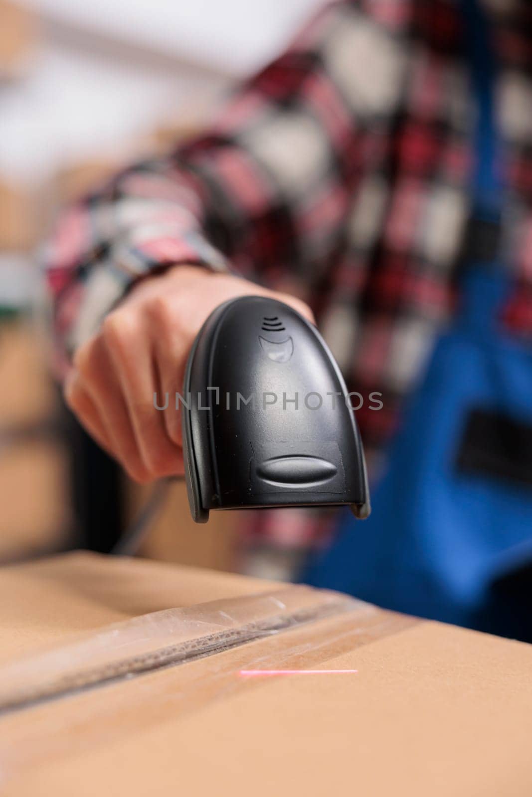 Delivery service employee scanning parcel and managing packages storing in warehouse. Storehouse worker doing shipment operations while holding barcode scanner in hand close up