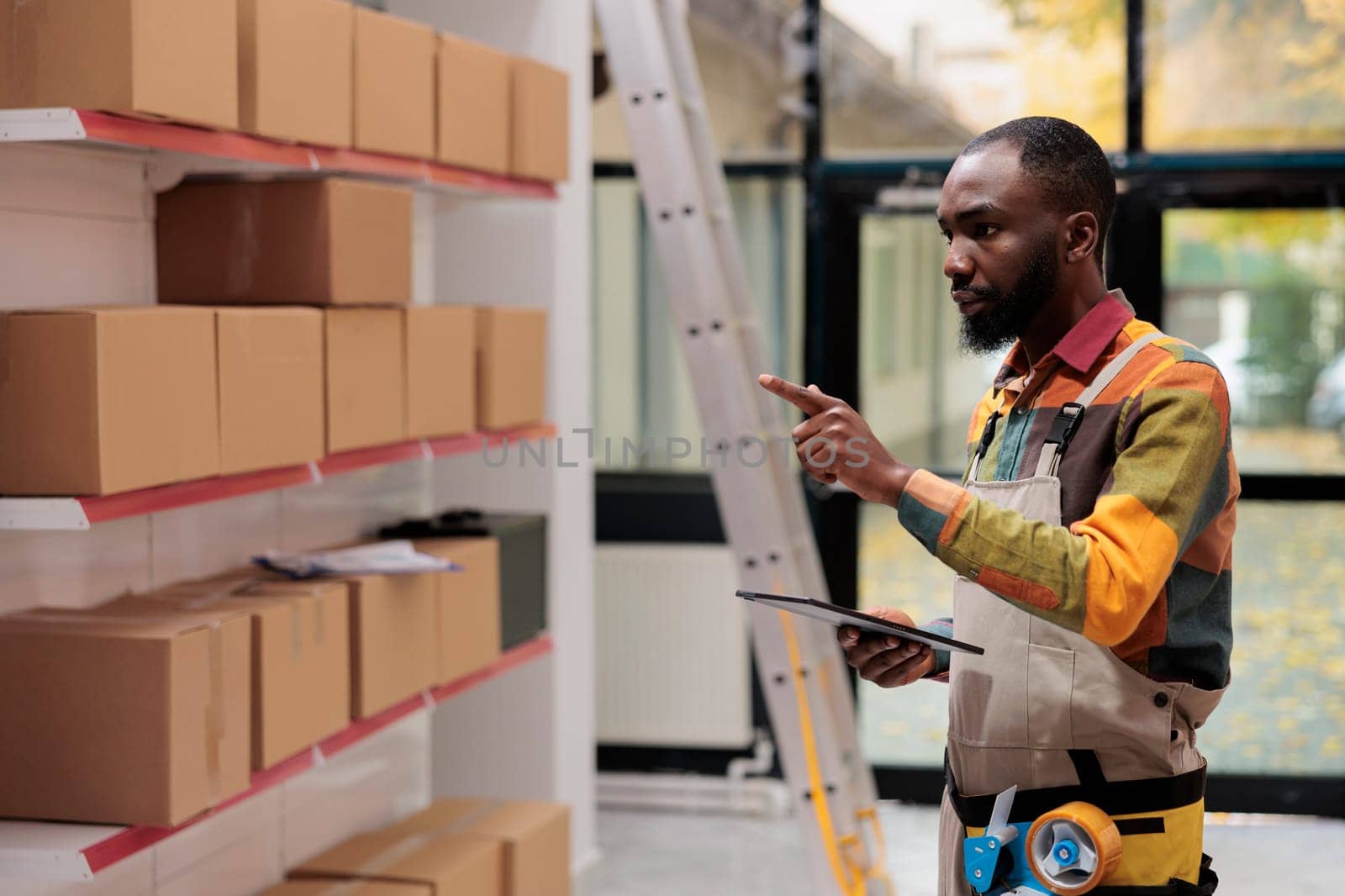 African american worker in industrial overall checking boxes, working at customers order preparing products for delivery in storehouse. Employee managing parcels transportation in warehouse