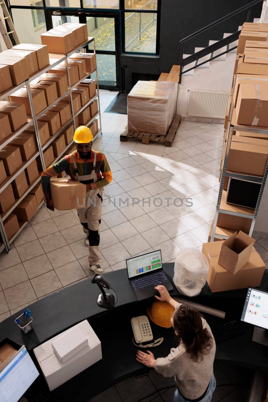 Top view of diverse employee working at products delivery in warehouse, preparing customers orders. Stockroom workers working at merchandise quality control at counter desk in storehouse