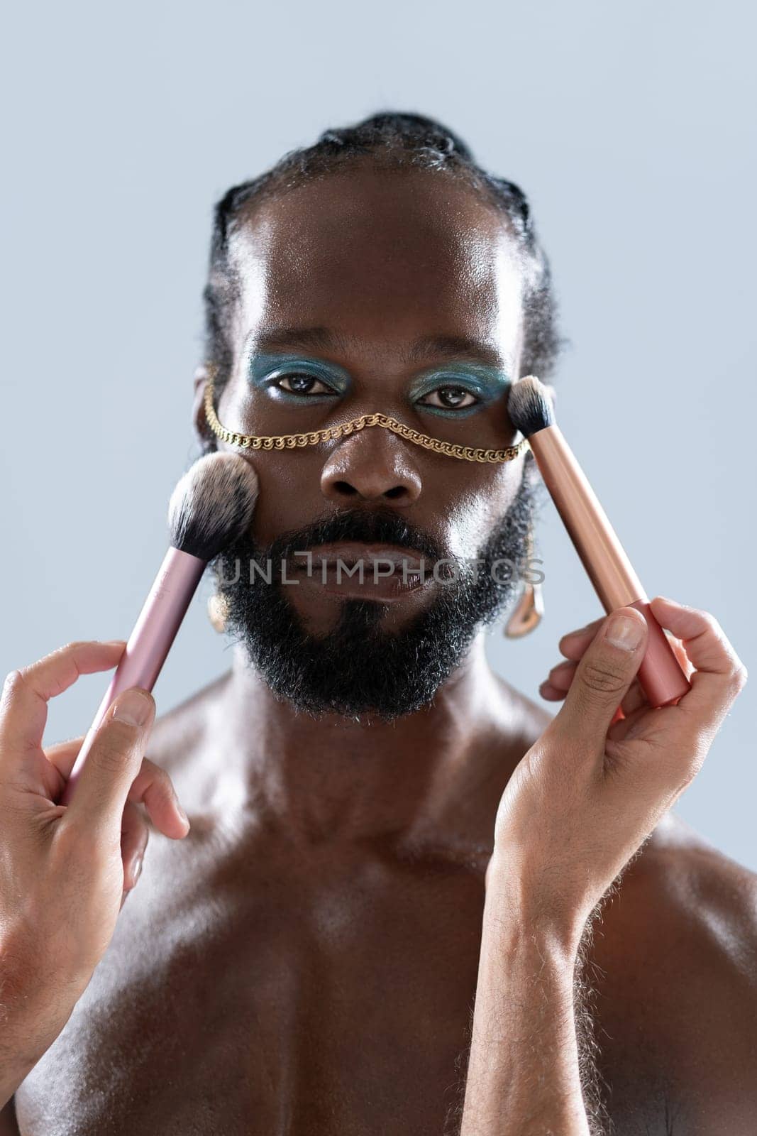 Bearded gay man applying makeup with brushes held by crop artist by andreonegin