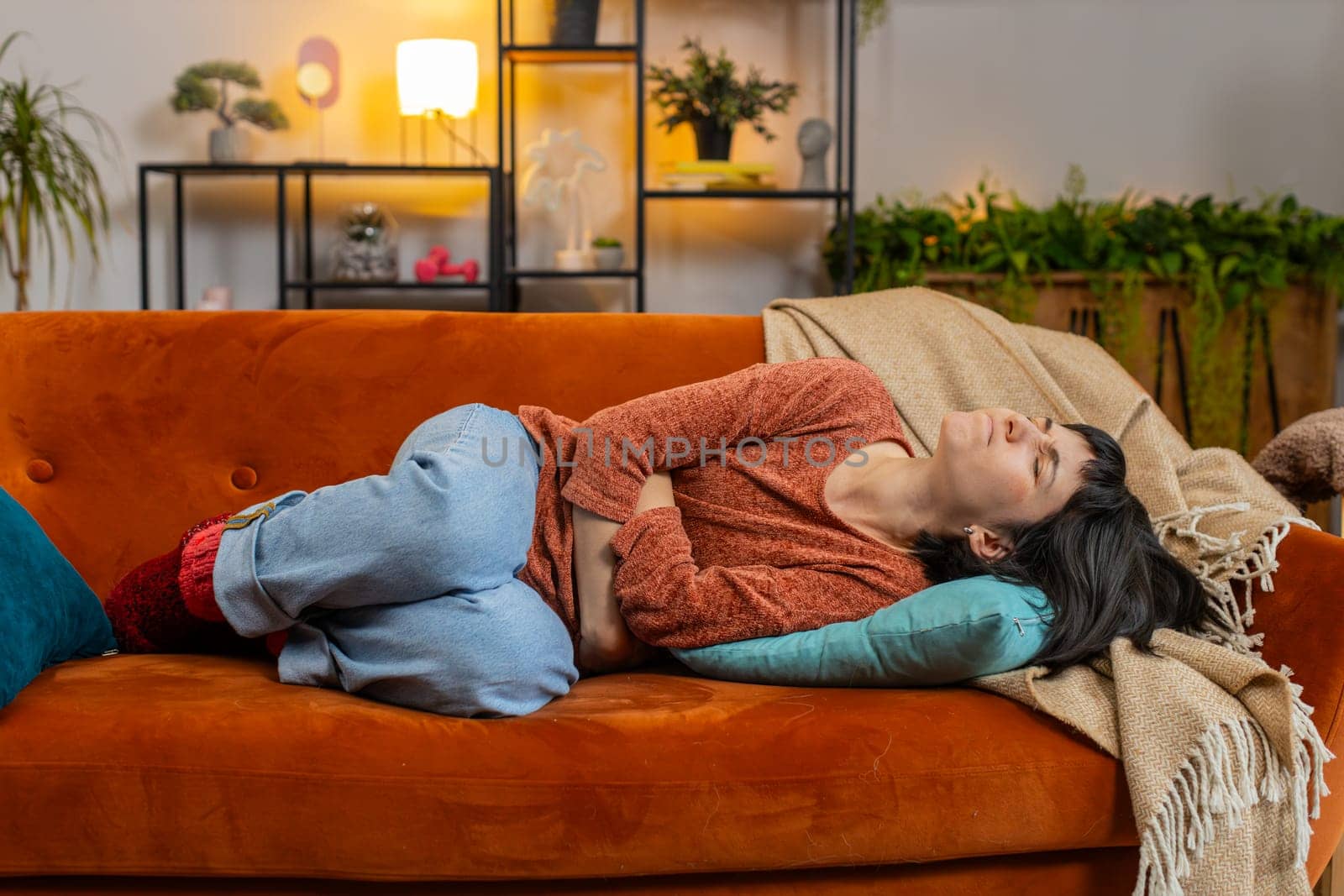 Upset young woman embracing belly suffering from stomachache lying on sofa. Unhappy Caucasian girl having menstrual painful feelings, resting on couch. Gastritis, abdominal or period pain concept