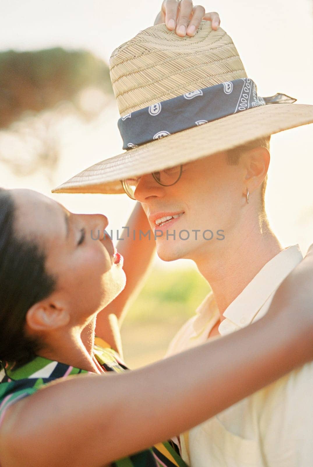 Young woman puts a straw hat on man head while hugging his neck by Nadtochiy