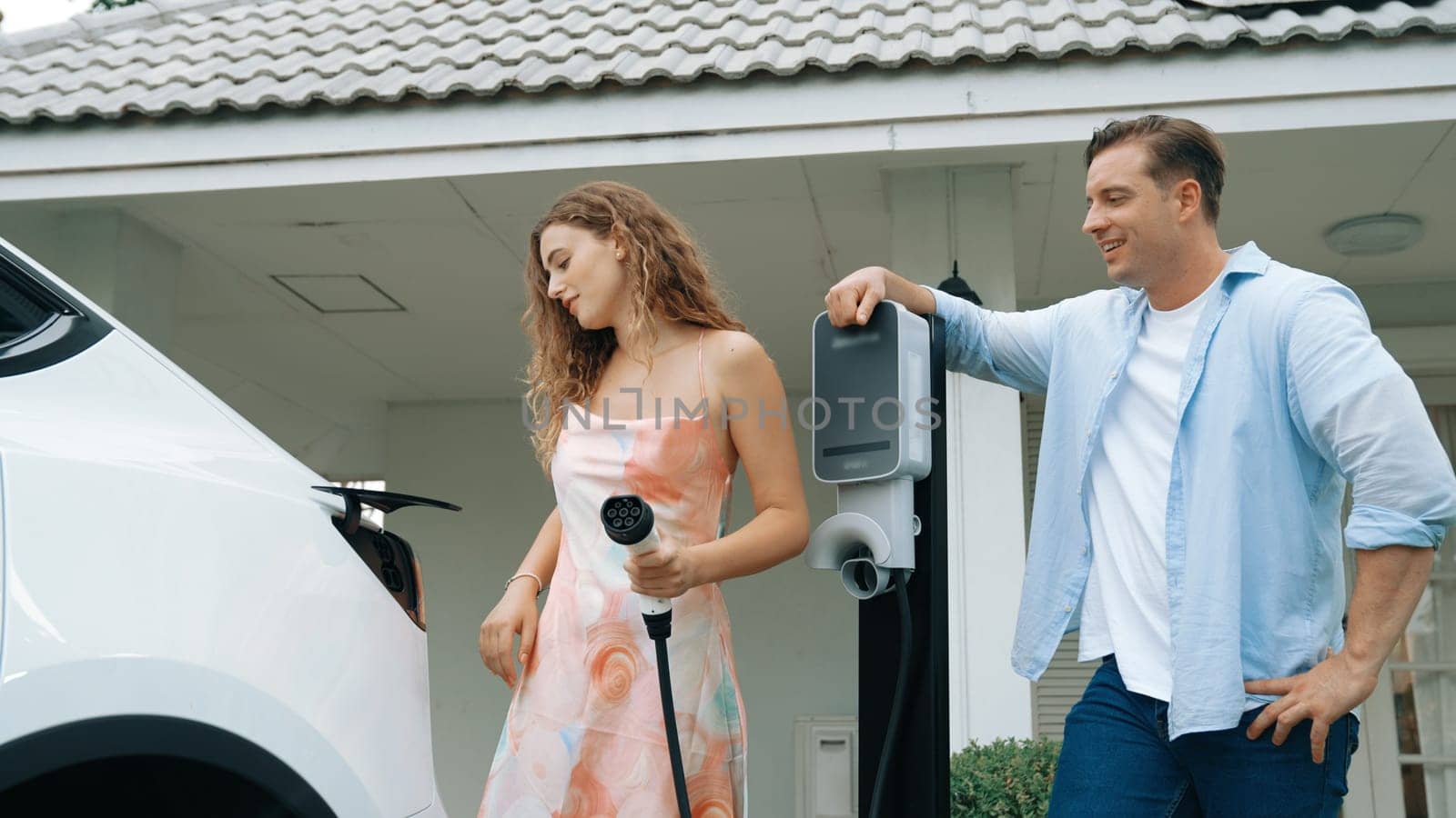 Happy couple recharge electric vehicle from EV charging station. Synchronos by biancoblue