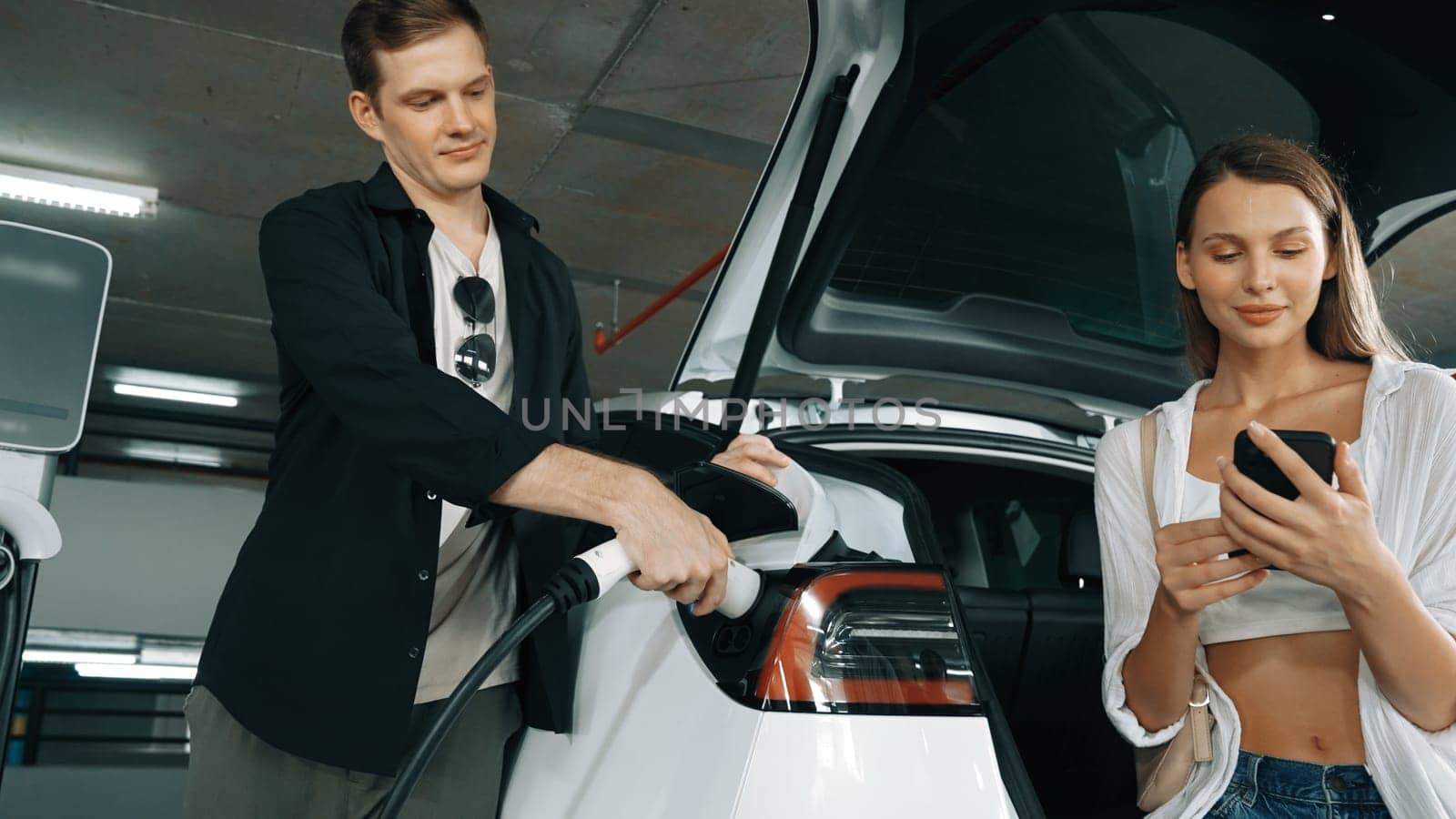 Electric car driver checks battery charging status app screen in car innards by biancoblue