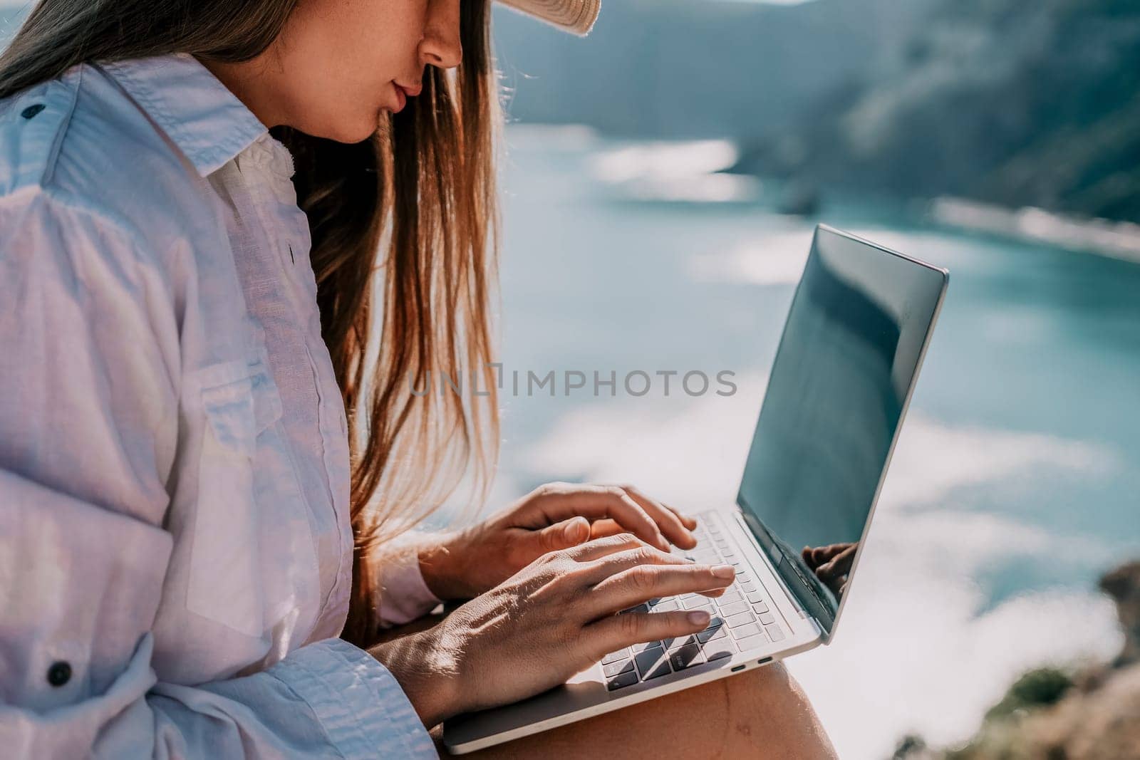 Woman sea laptop. Business woman in yellow hat freelancer with laptop working over blue sea beach. Girl relieves stress from work. Freelance, digital nomad, travel and holidays concept by panophotograph