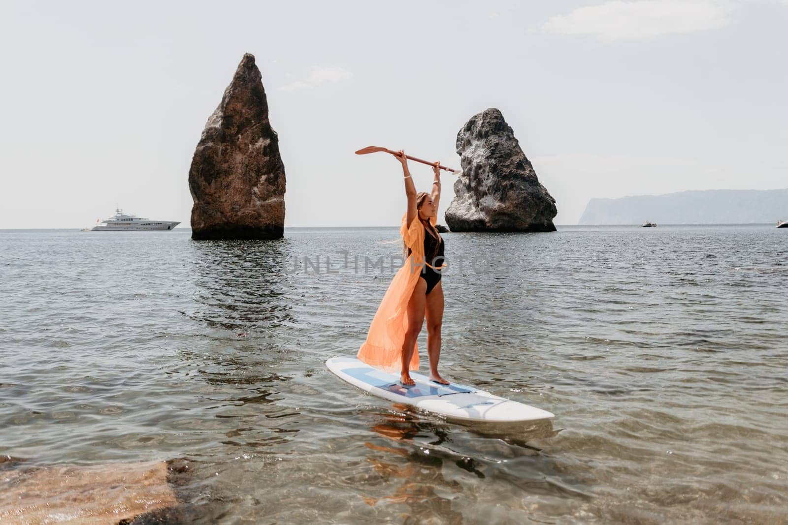 Close up shot of beautiful young caucasian woman with black hair and freckles looking at camera and smiling. Cute woman portrait in a pink bikini posing on a volcanic rock high above the sea