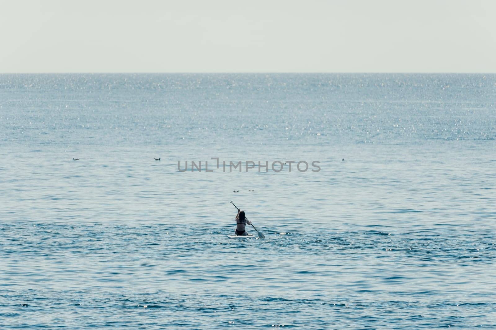 Sea woman sup. A happy positive woman in hat with family relaxing in sea, aerial back view of family on SUP board floating on calm water. Active lifestyle at sea. Summer vacation. Slow motion