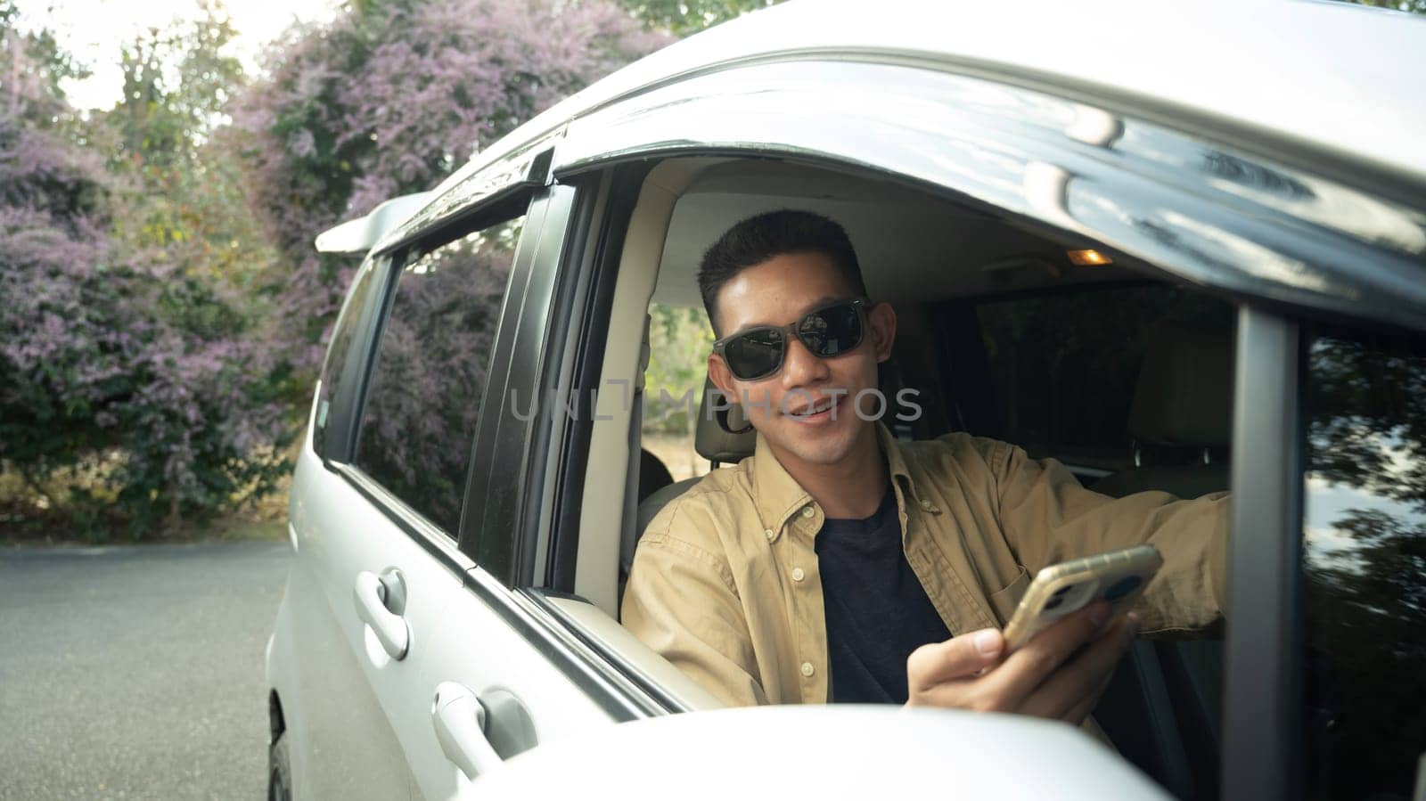 Smiling man in sunglasses using mobile phone while driving on country road. Traveling and lifestyle concept.