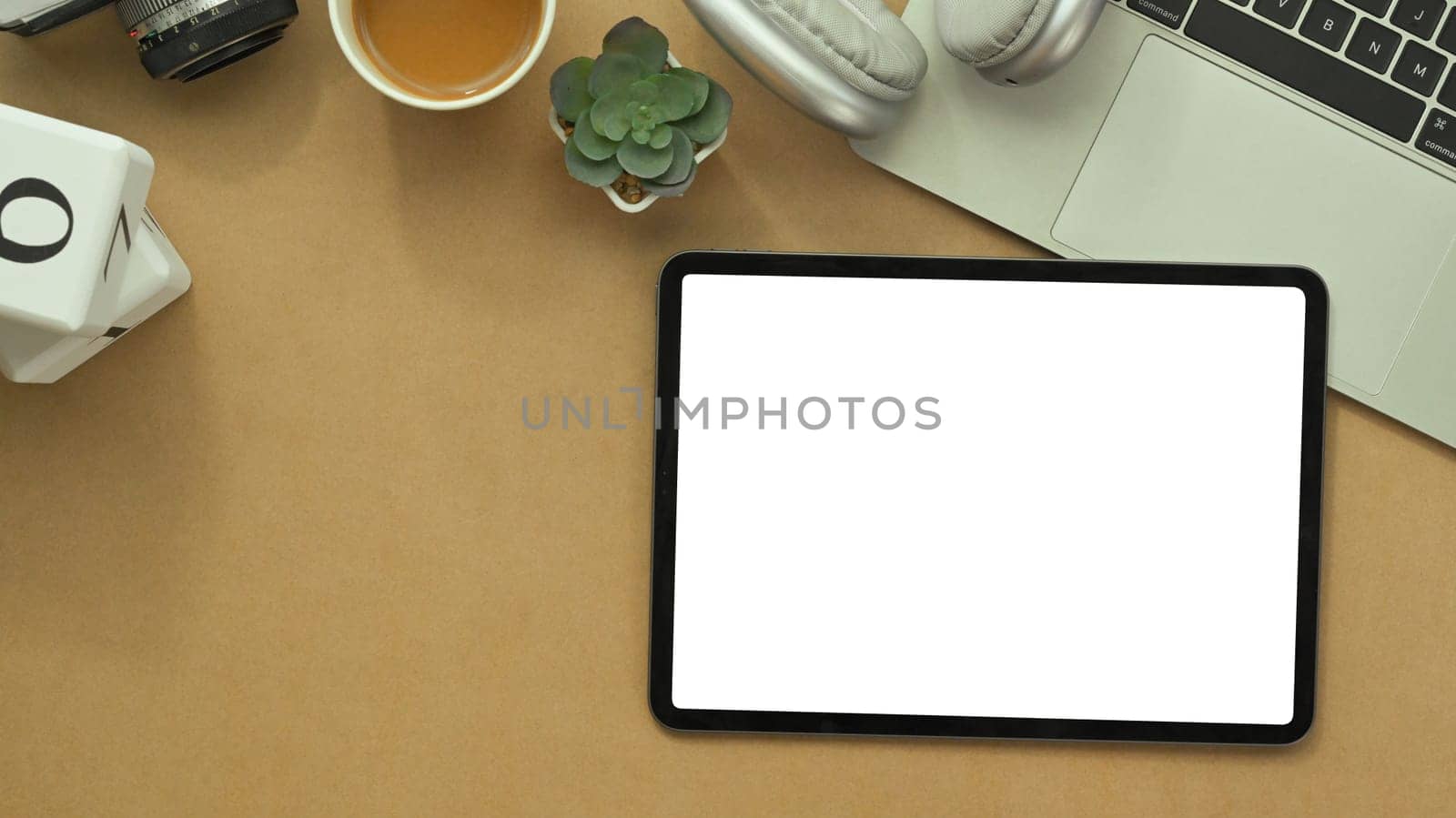 Digital tablet with white blank screen, laptop, notepad and headphone on brown background.