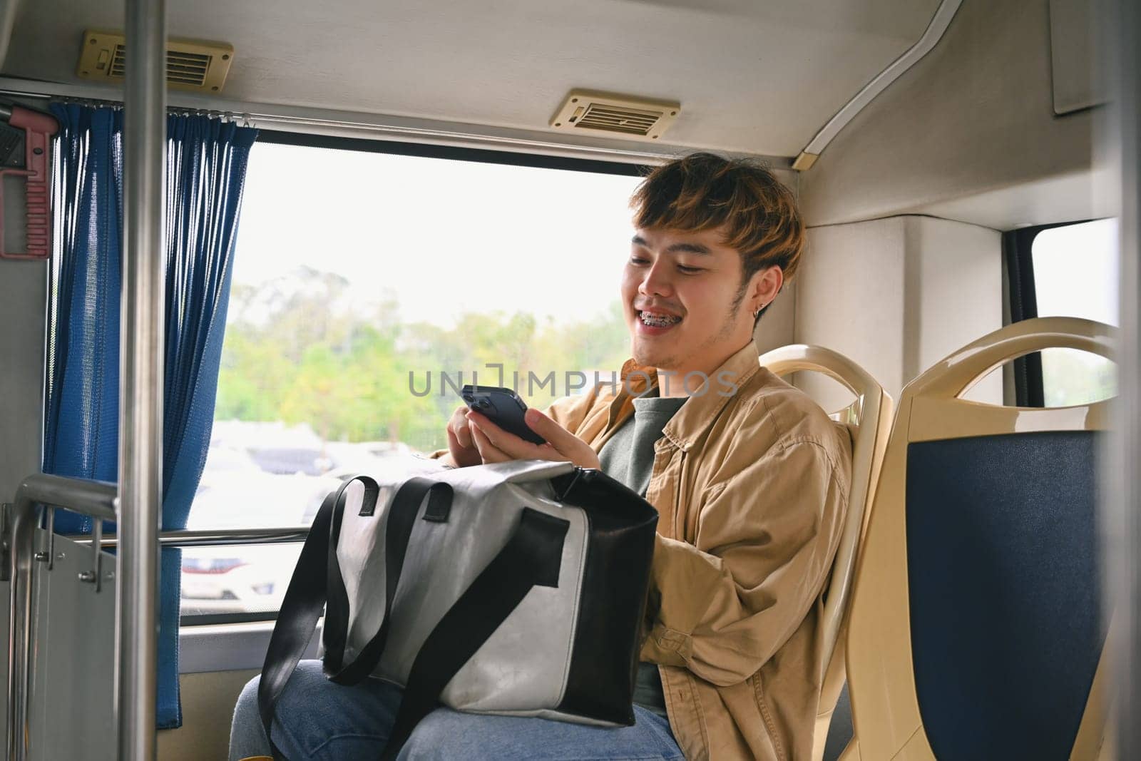 Happy young man tourist using a smartphone in public transportation. People and transportation concept by prathanchorruangsak