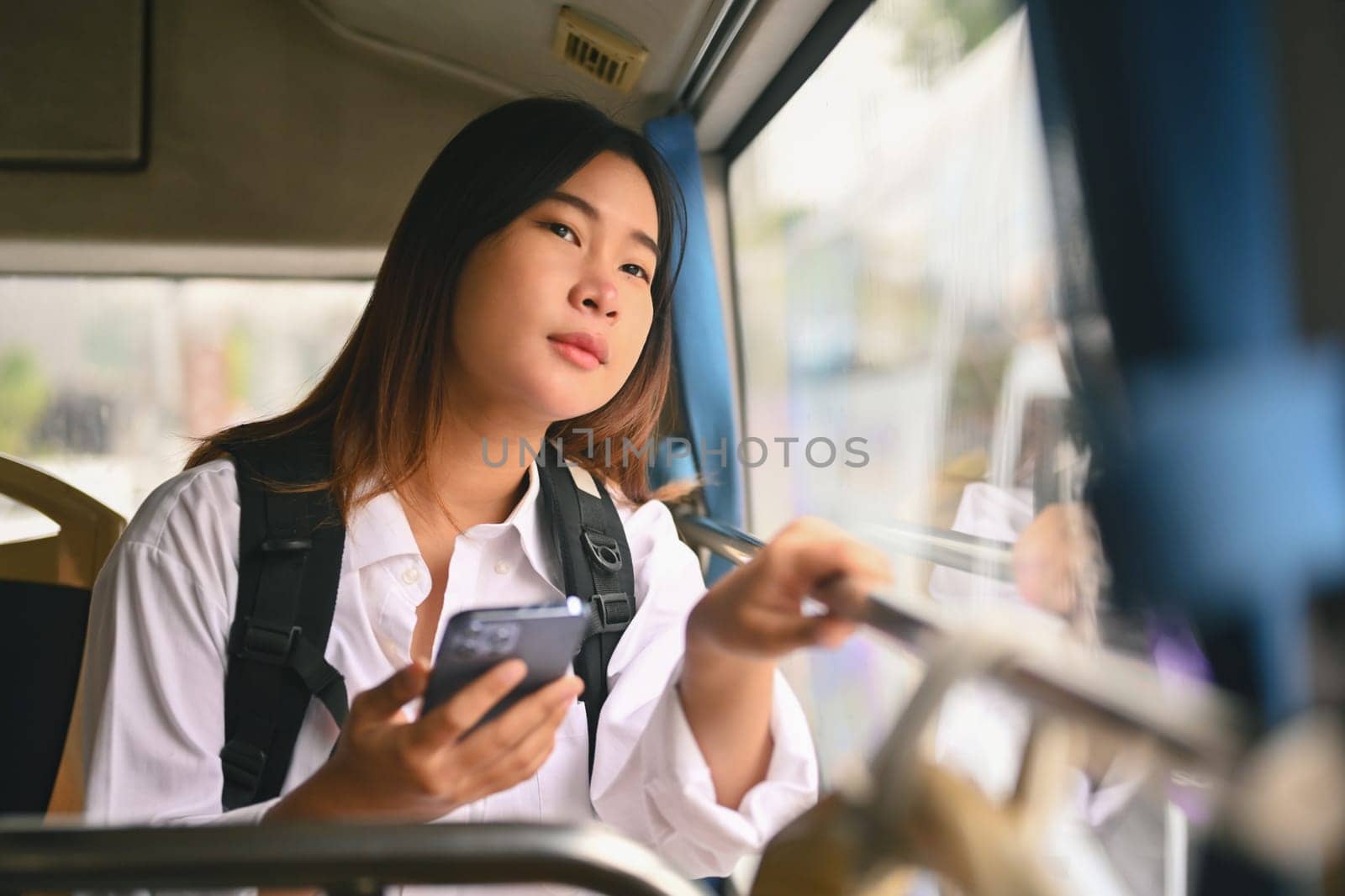 Pretty young woman sitting inside public bus and looking through the window by prathanchorruangsak