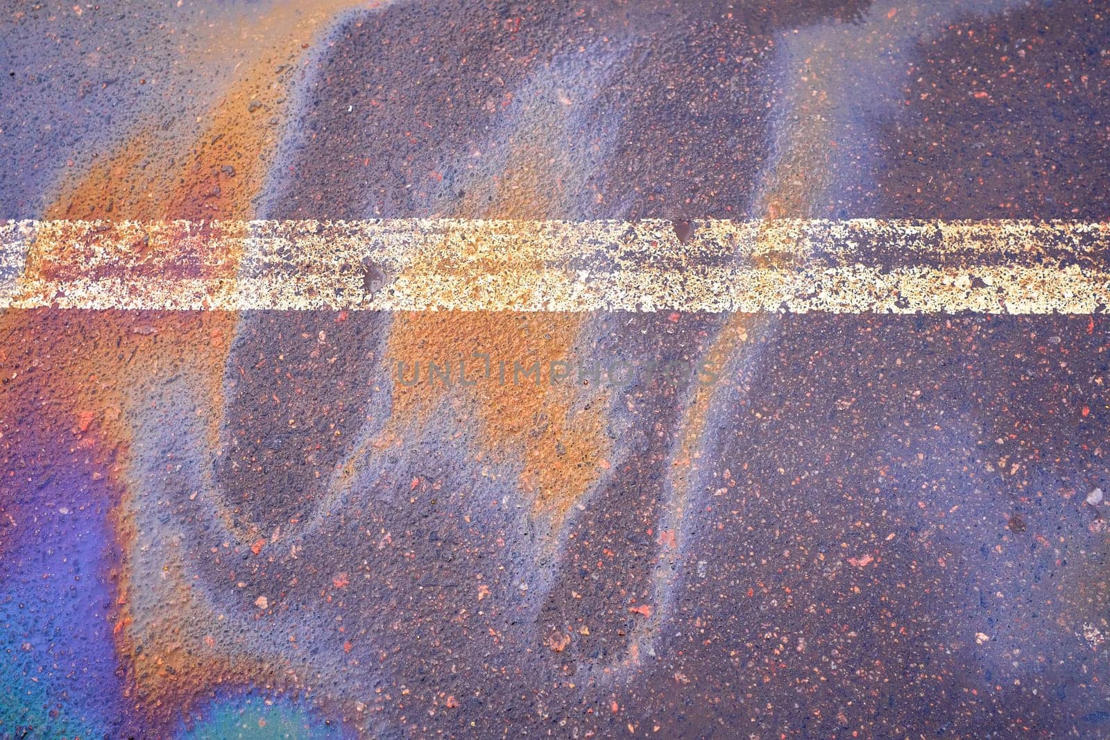 Oil spill on wet asphalt, parking lot with dividing line.