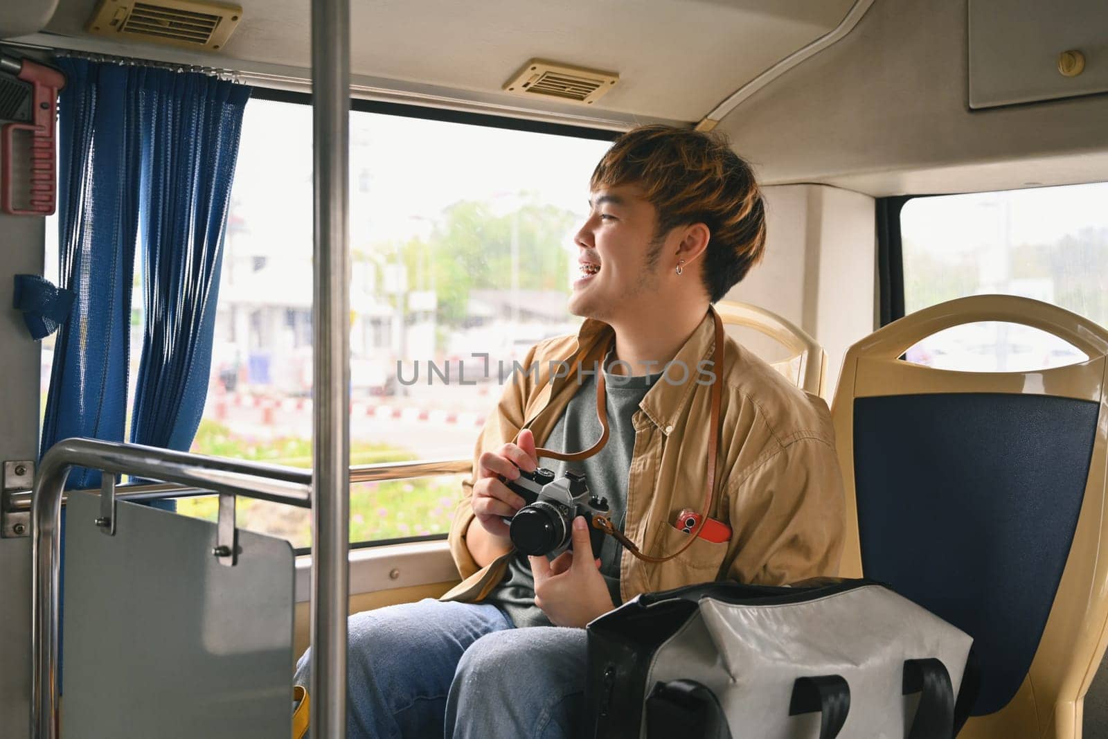 Smiling young Asian man commuting by public transportation and looking through the window.