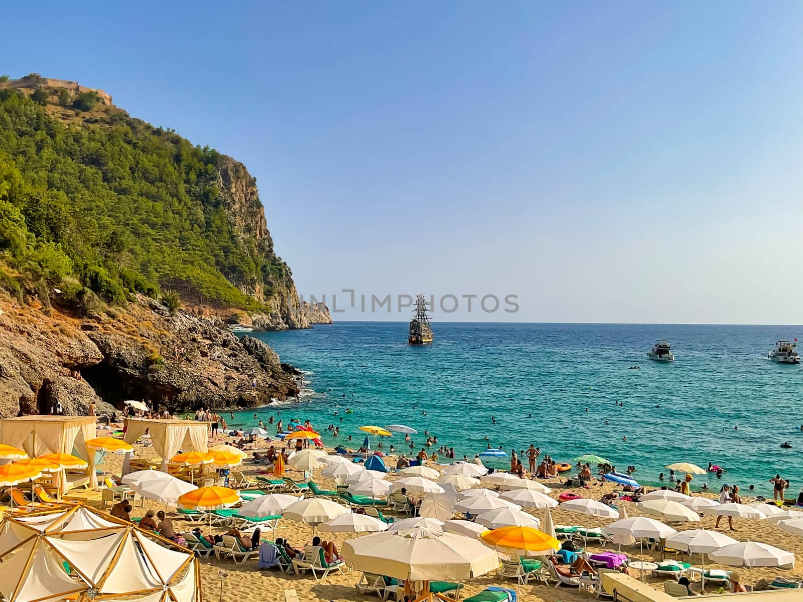 Cleopatra beach in Alanya with beach umbrellas, people and mountain view. Sunny day on the beach. High quality photo