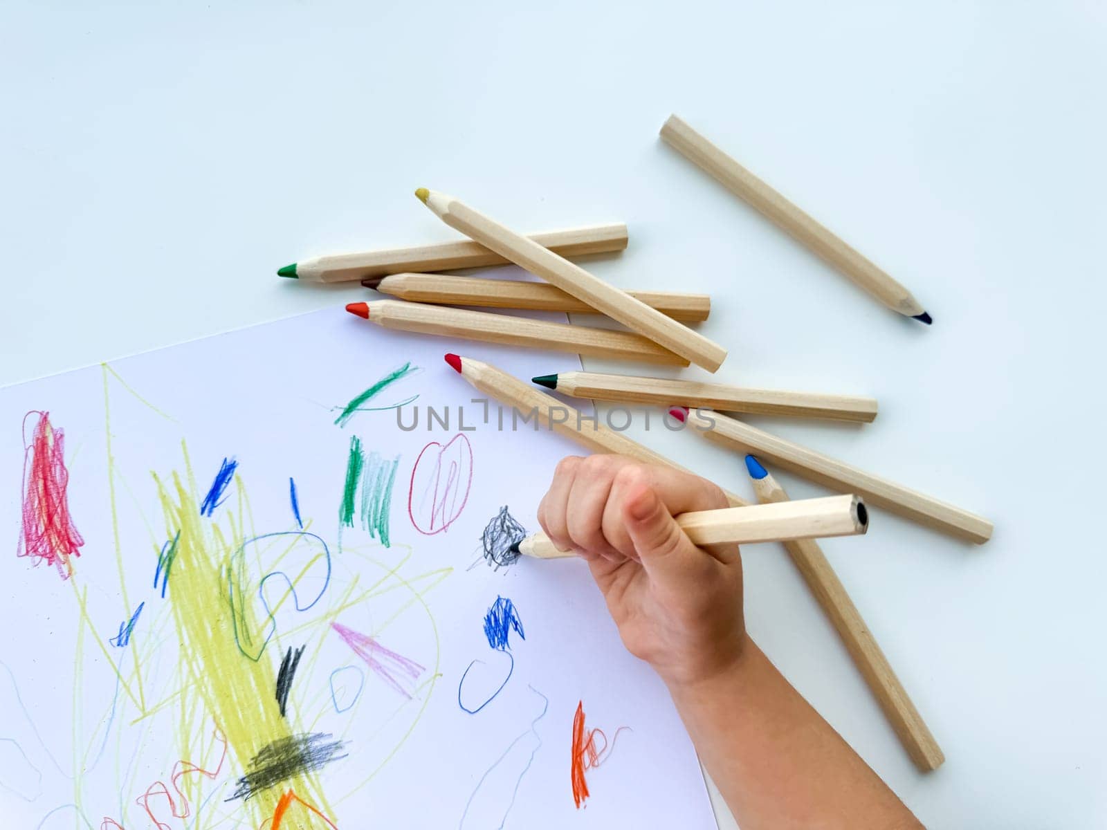 small child draws with colored pencils on paper on white table. High quality photo