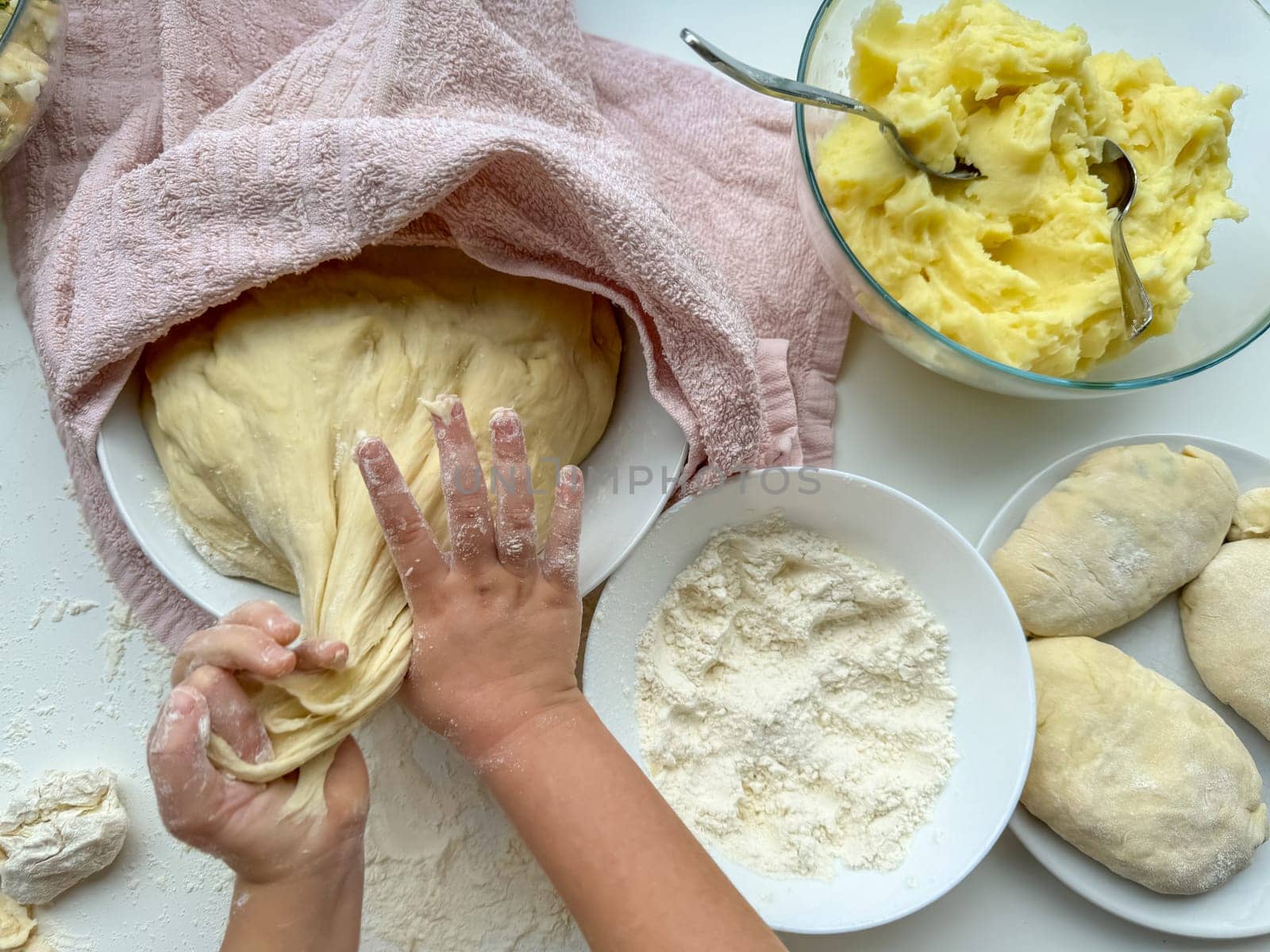 The hands of child knead the dough for making pies on white table, top view. High quality photo