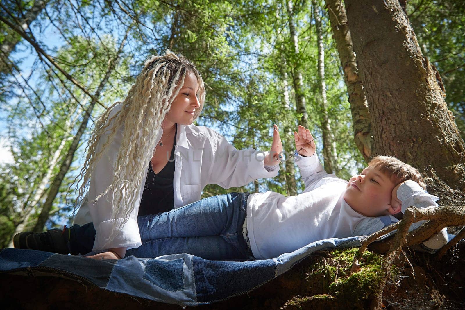 Funny mother with dreadlocks and fat boy happy resting in forest on a sunny summer day