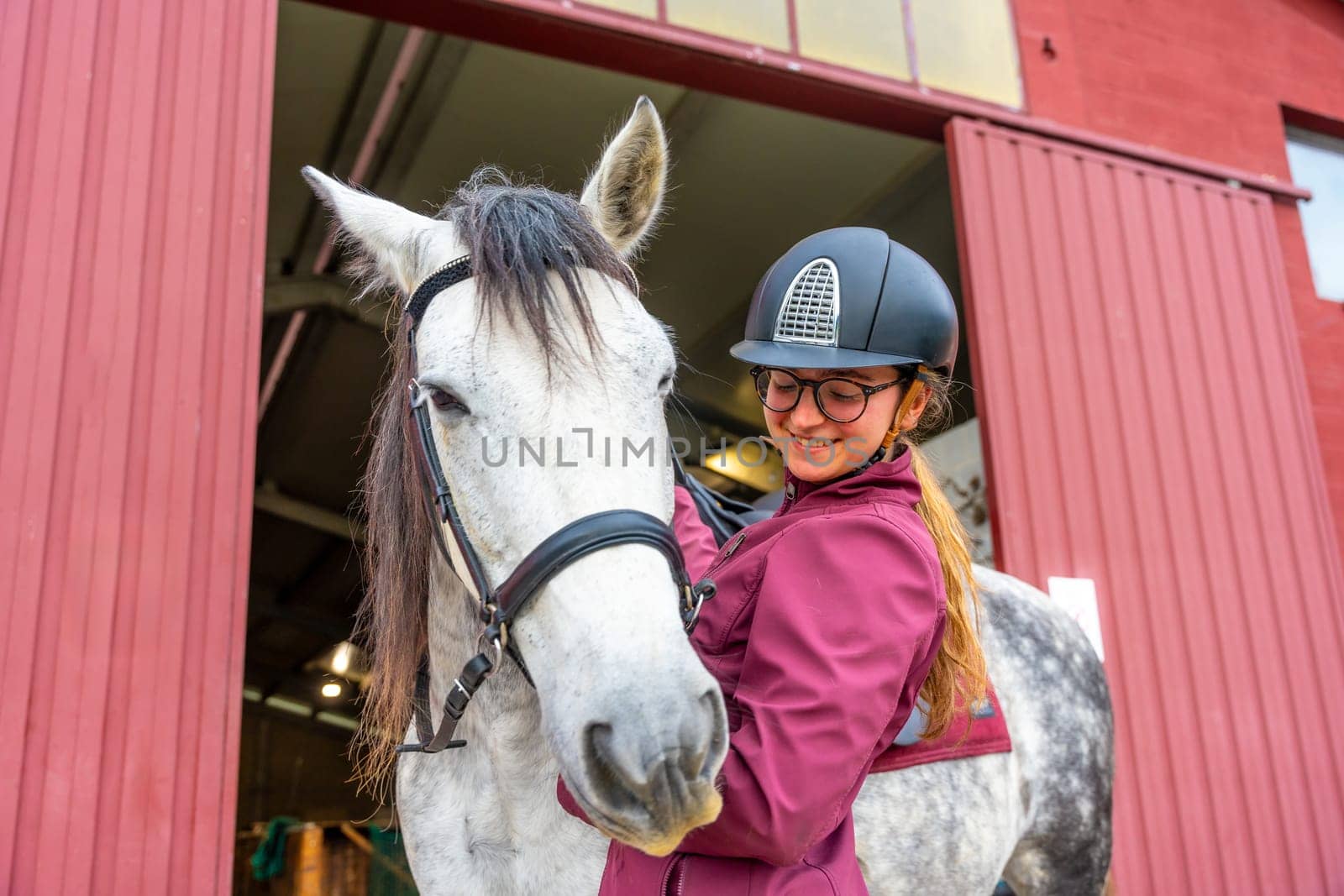 Low angle view photo of a female young jockey caressing her horse outside the stable