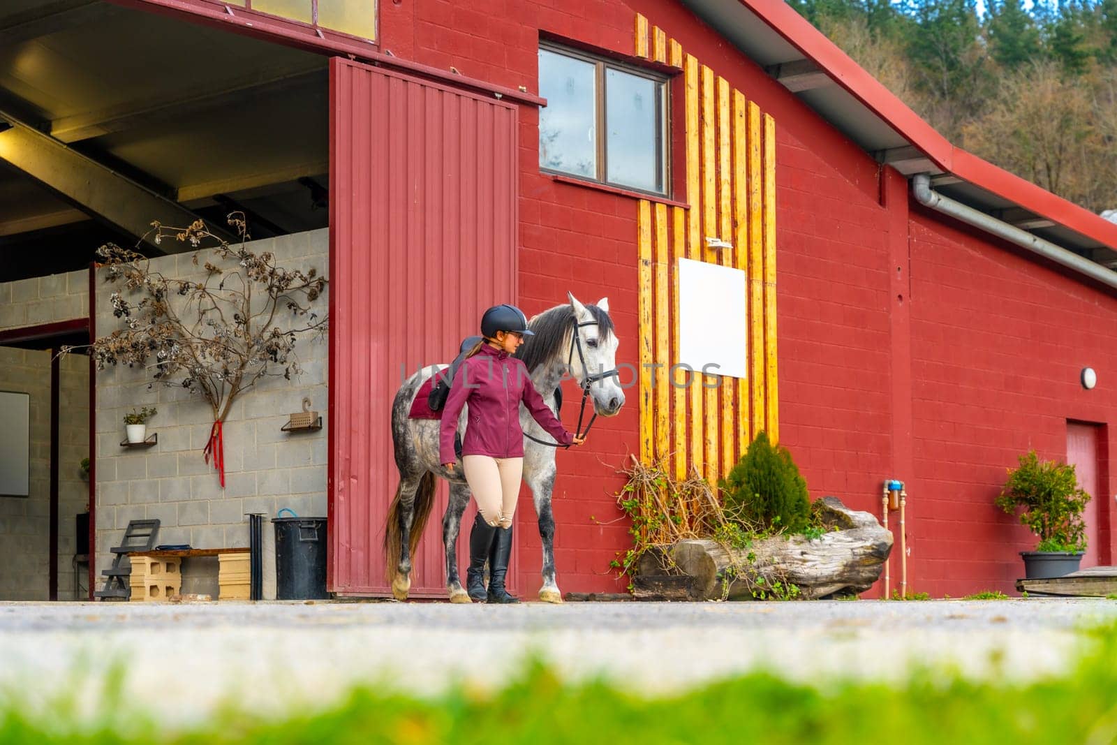 Wide view photo of a young female trainer and horse coming out a stable
