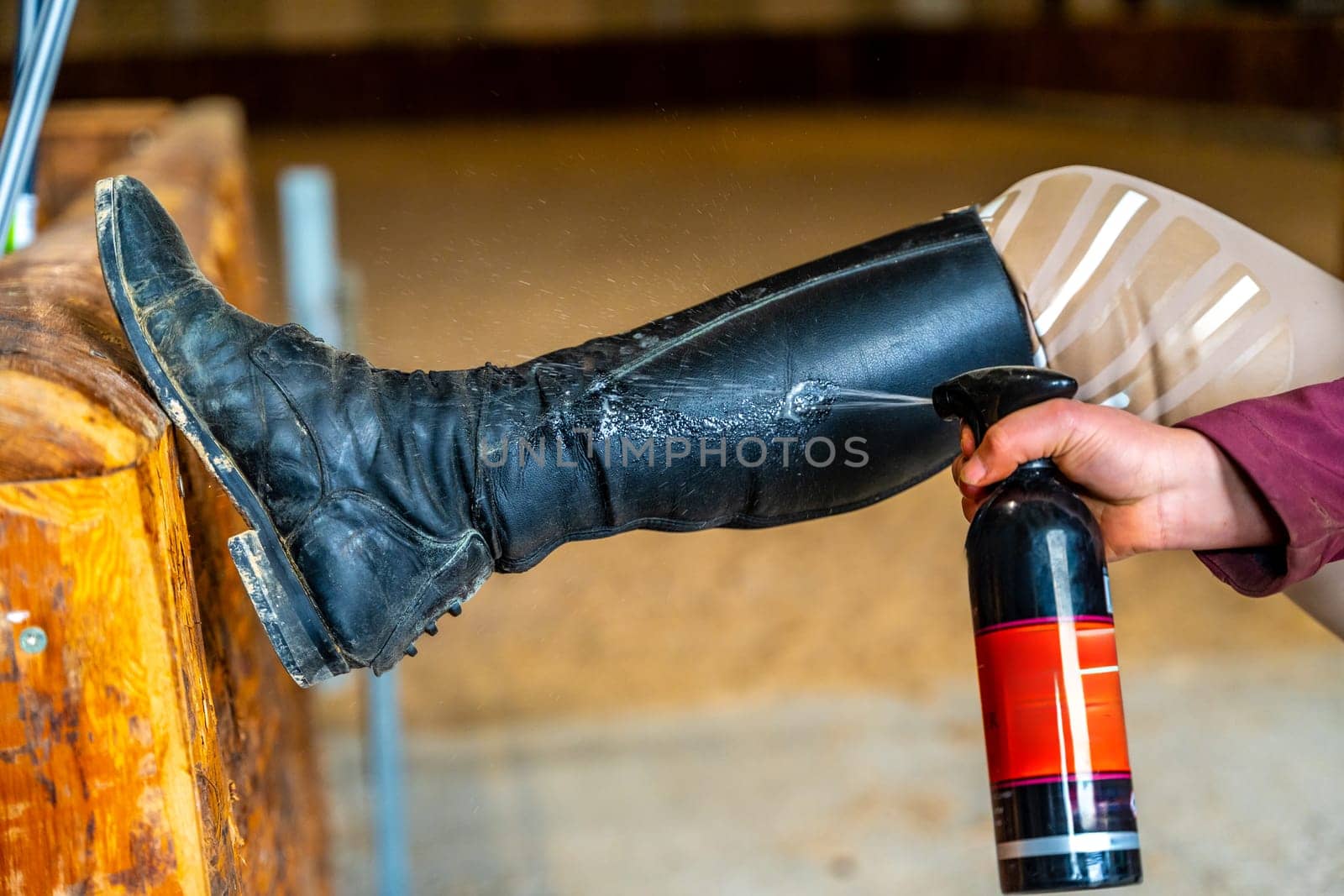 Cropped photo of the hand of a woman cleaning horse riding boots with spray