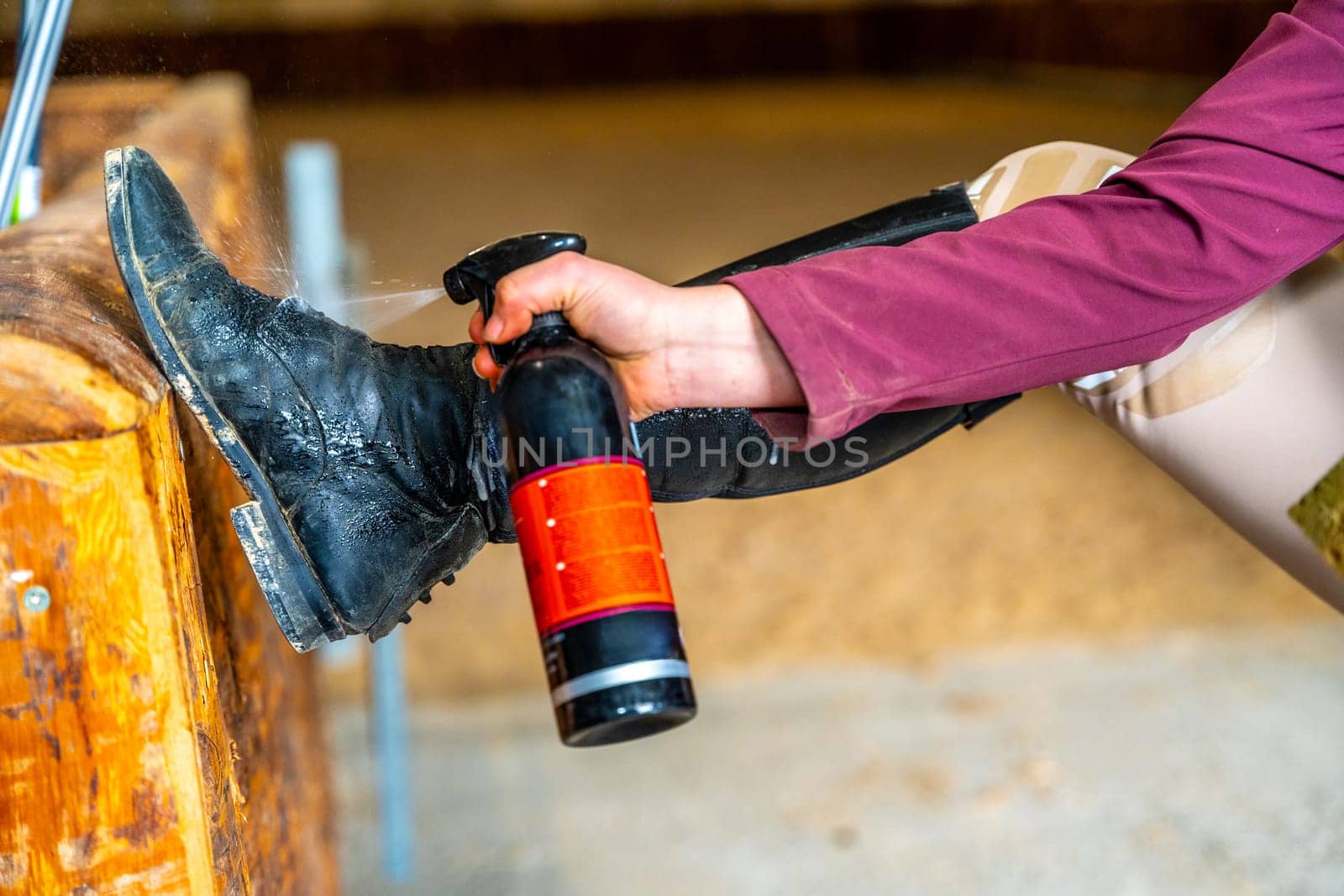 Part of a woman cleaning riding boots with spray in a ranch