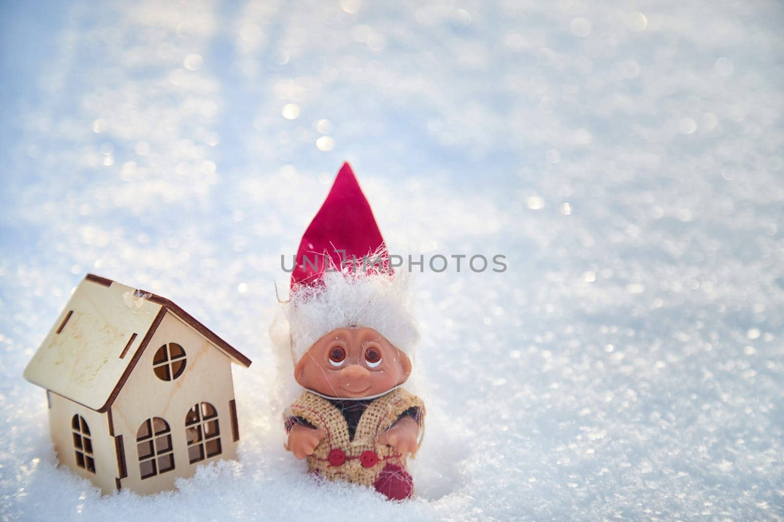 Cute little funny dwarf and small wooden house in snow in winter landscape. Wizard on snowy background. Christmas and New Year