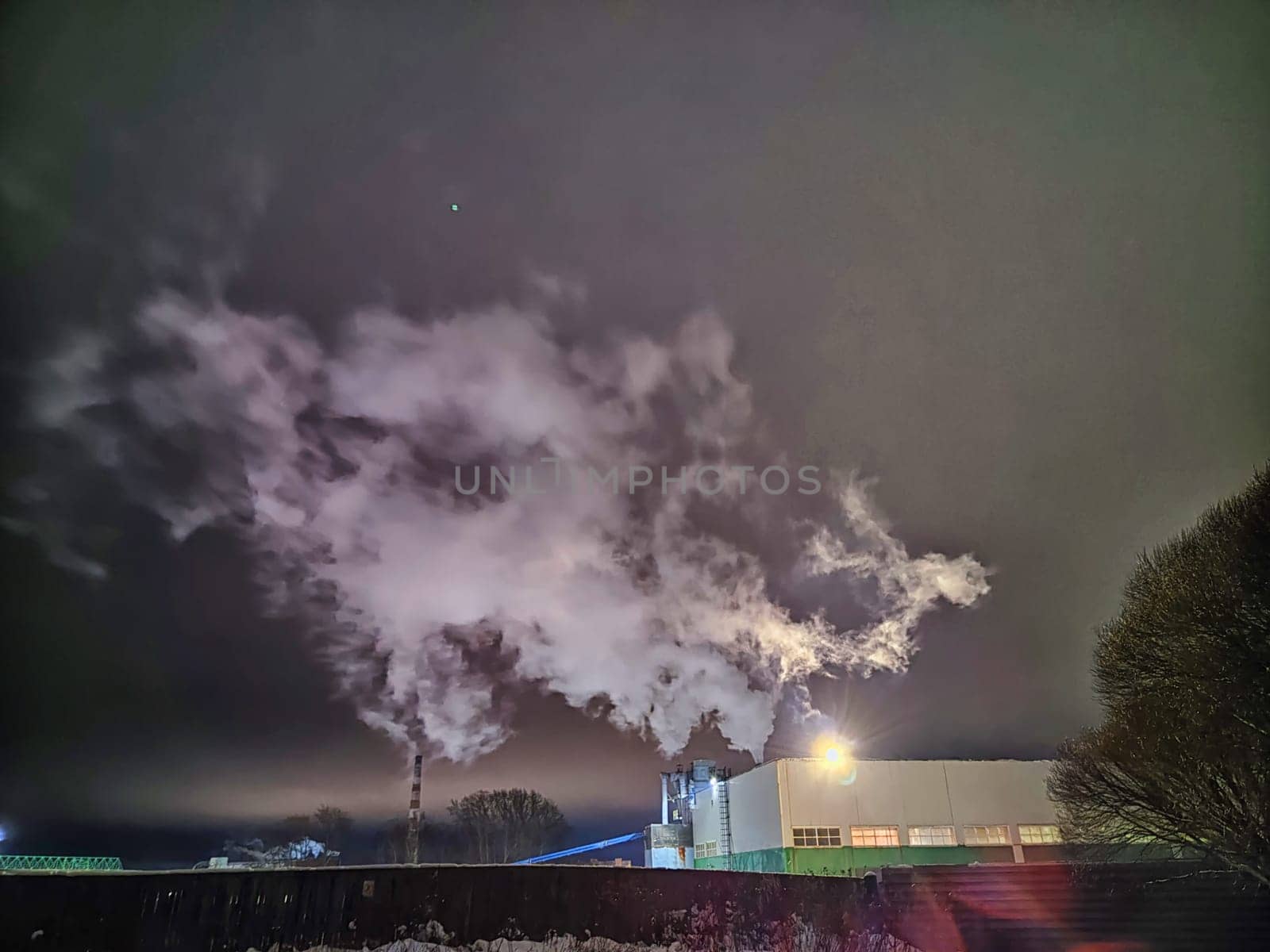 White smoke from the chimney against the dark sky at night with backlight. Chimneys, concept of industry, ecology, heating season, global warming