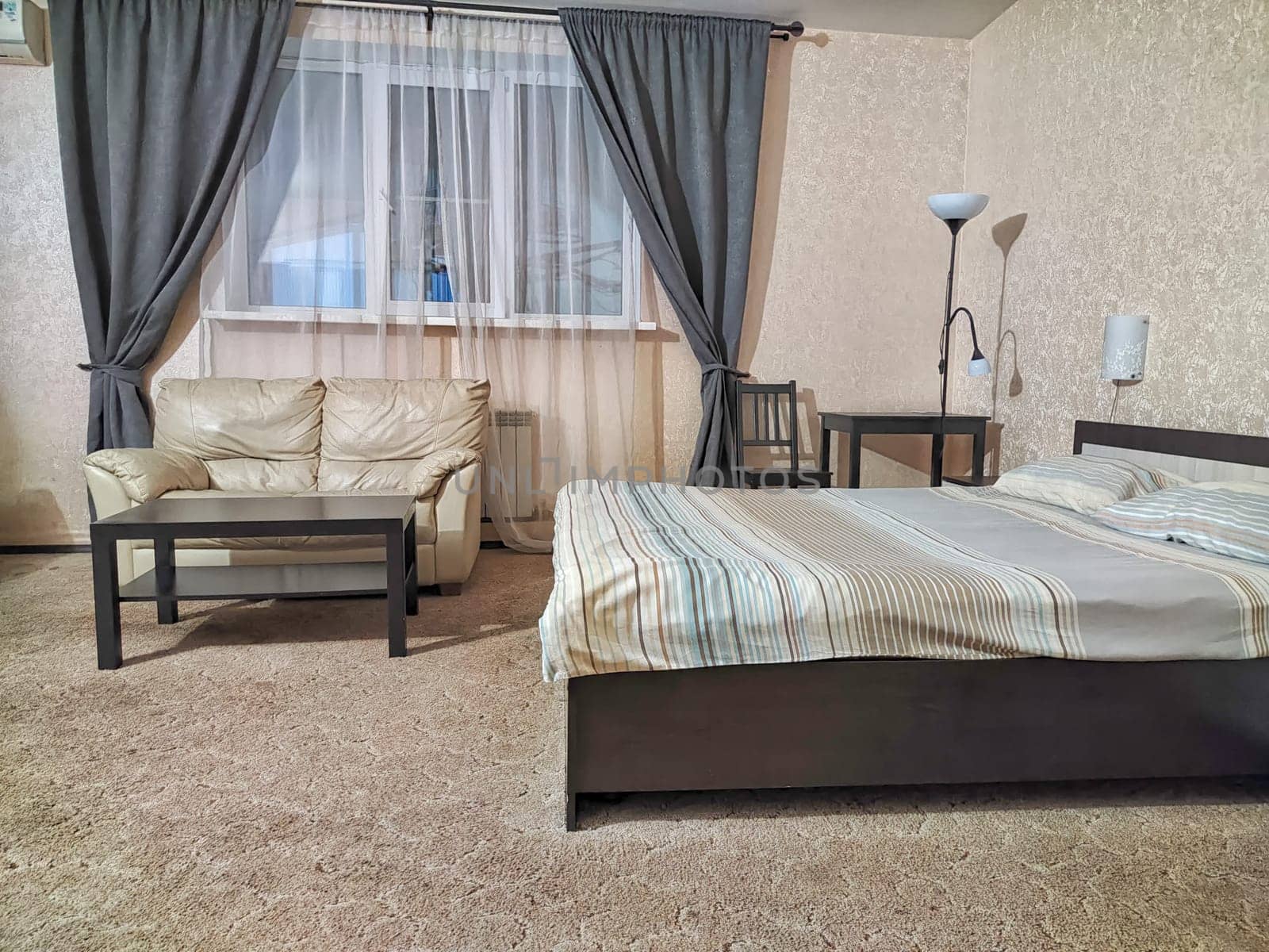 Stylish bedroom in beige tones and colors with double bed, sofa, table. Concept of cozy bedroom, living room or hotel room