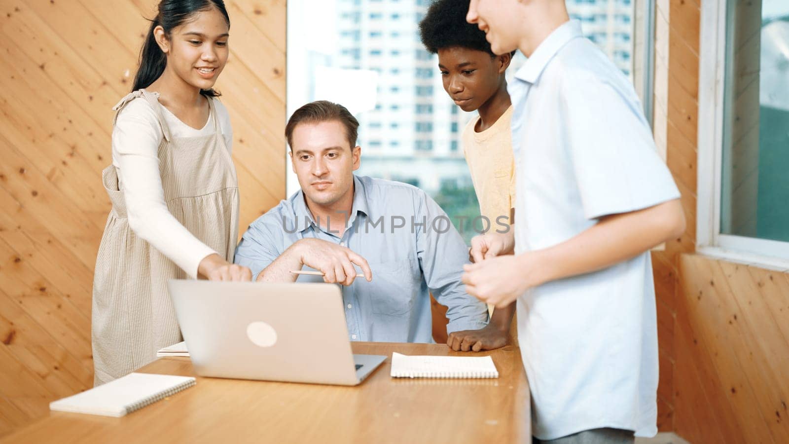 Highschool boy presenting project while teacher looking at laptop. Group of diverse student standing and explain plan while smart instructor listening and giving advise.Teamwork concept. Edification.