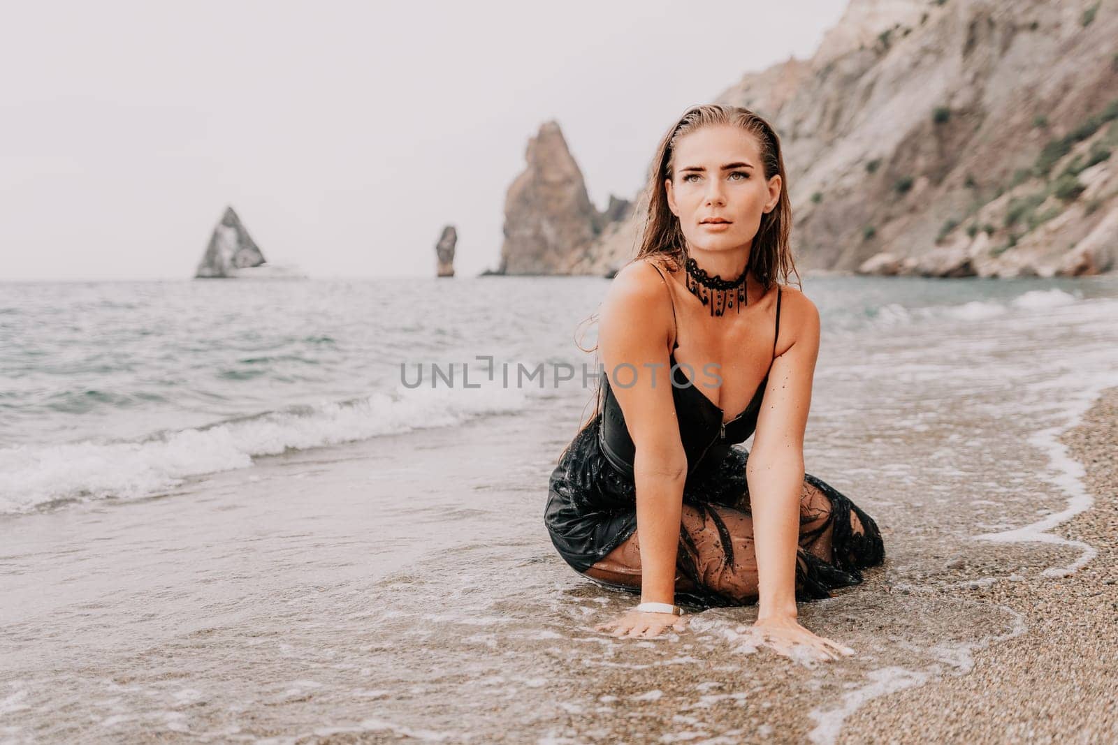Woman summer travel sea. Happy tourist in black dress enjoy taking picture outdoors for memories. Woman traveler posing on sea beach surrounded by volcanic mountains, sharing travel adventure journey by panophotograph