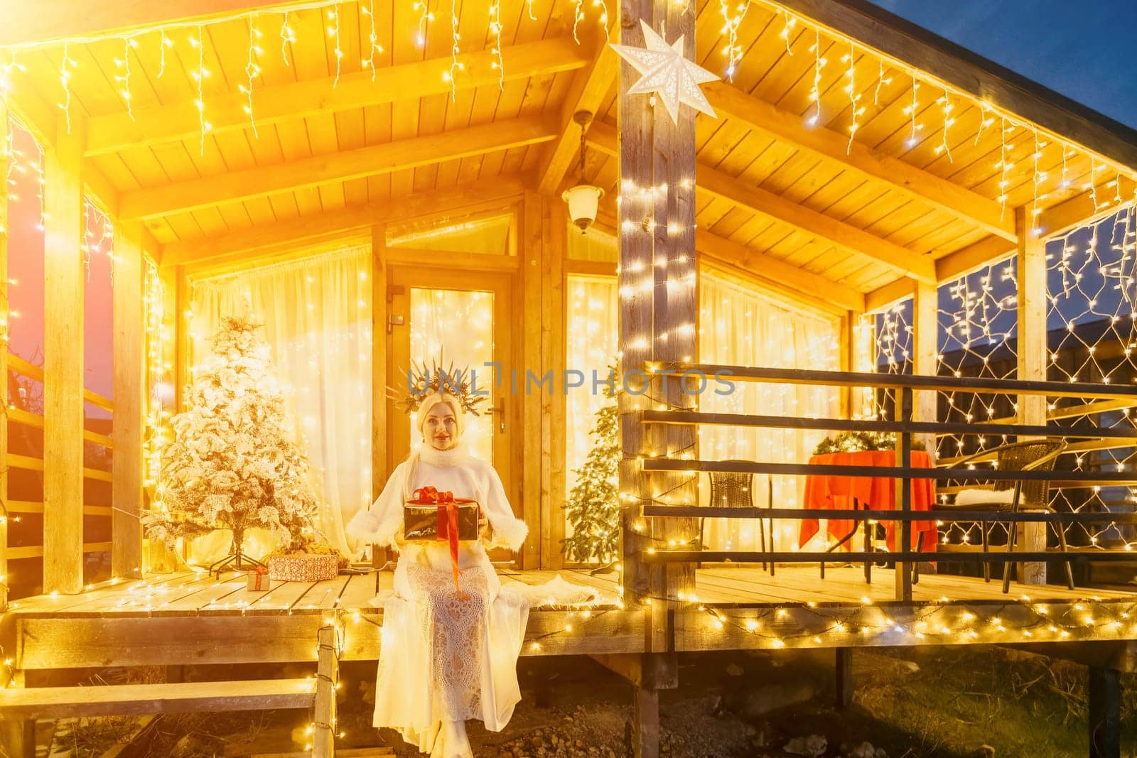 Happy smiling woman in a white dress holding a gift box in front of a Christmas tree. by panophotograph