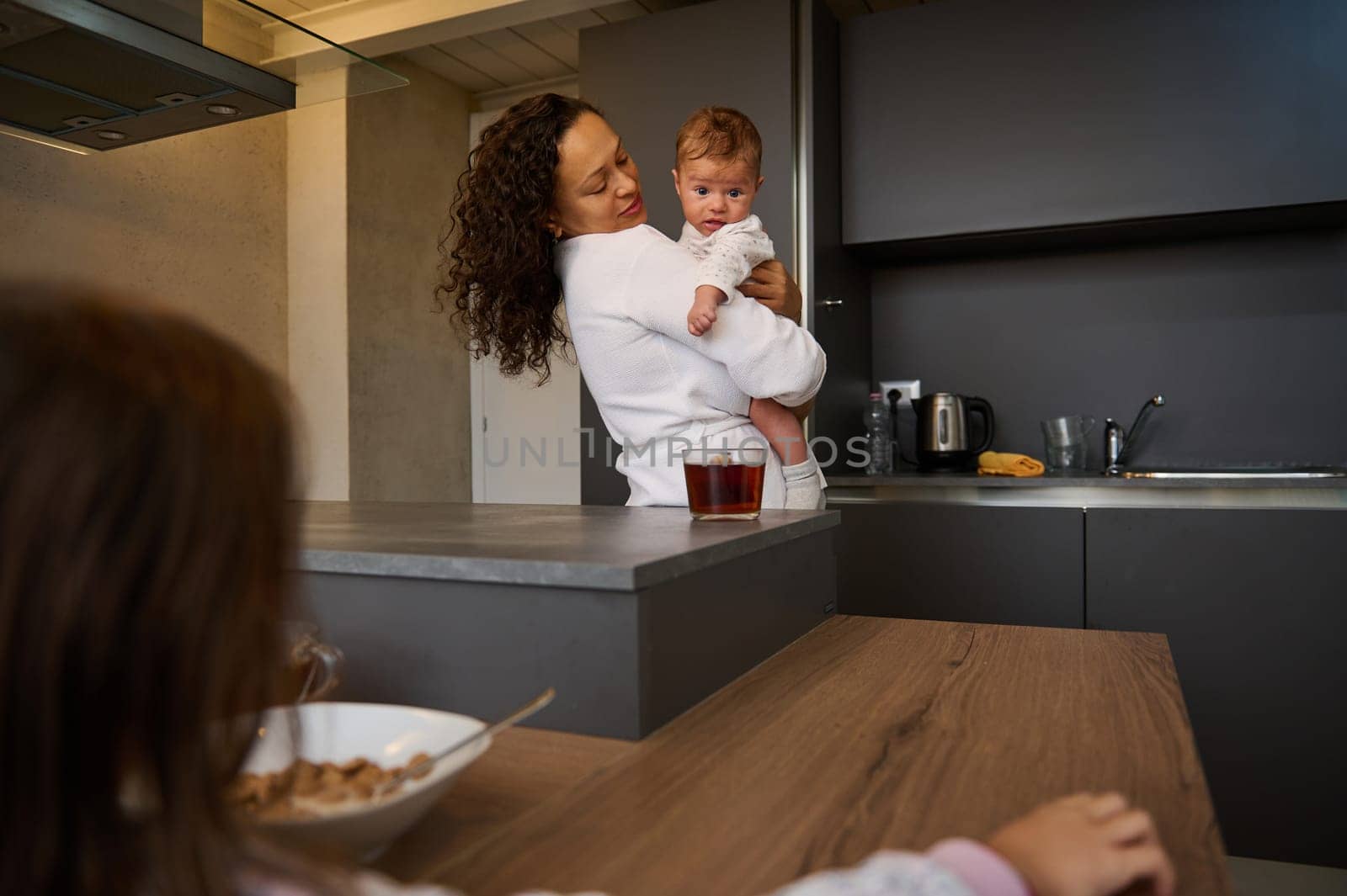 Selective focus of a young mother holding baby boy, son while older daughter sitting near bowl with delicious flakes by artgf