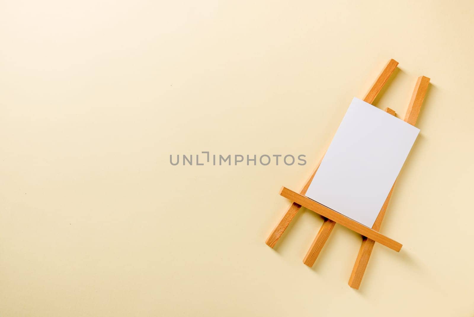 Small wooden easel with blank photo card on yellow background