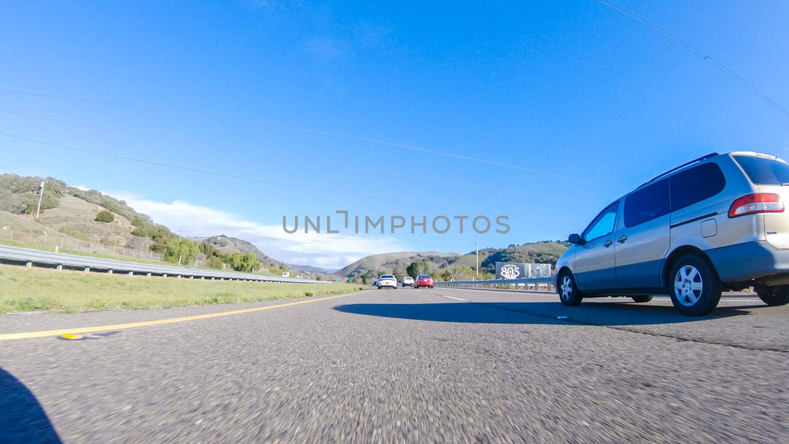Santa Maria, California, USA-December 6, 2022-On a crisp winter day, a car cruises along the iconic Highway 1 near San Luis Obispo, California. The surrounding landscape is brownish and subdued, with rolling hills and patches of coastal vegetation flanking the winding road.