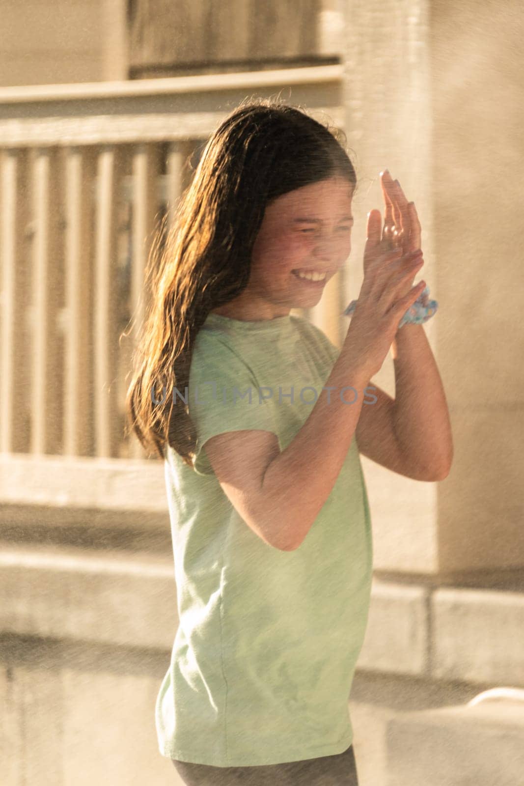 A joyful young girl gleefully gets soaked in refreshing water mist during a hot summer day.