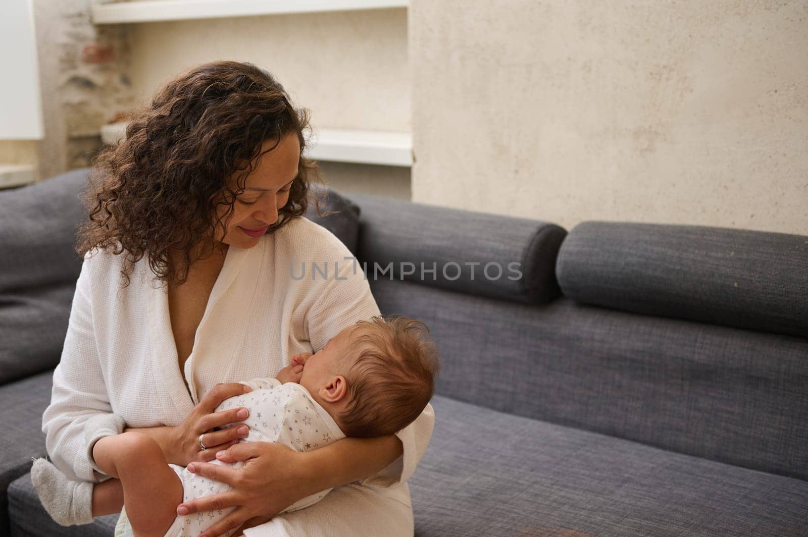 A radiant young adult happy and affectionate mother holding a sleeping baby boy in her arms. Mother hugging her little child. Maternity leave lifestyle. Babyhood and infancy. Family relationships