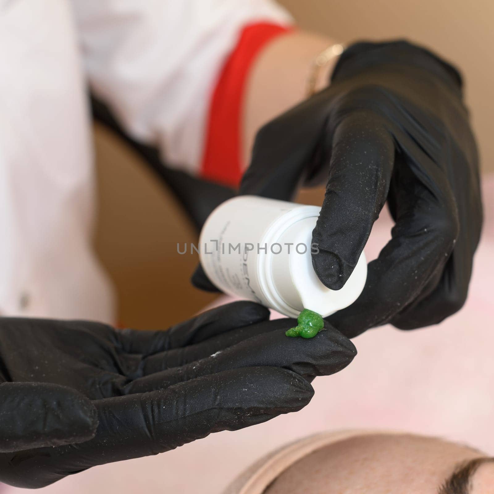 Ivano-Frankivsk, Ukraine May 17, 2023: A beautician applies a green mask to a girl's face, carboxytherapy cosmetology procedure, a beautician in black gloves.