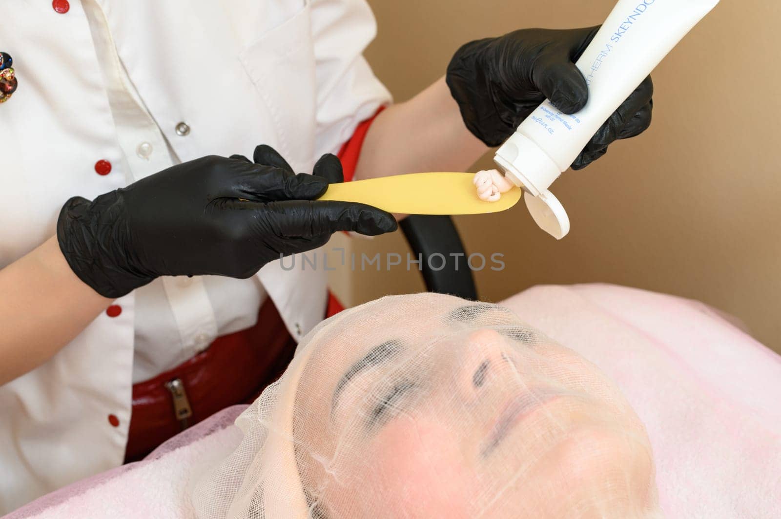 A beautician uses a spatula to apply cream to an already prepared face with gauze, a procedure for facial skin with couperosis. Ivano-Frankivsk, Ukraine May 17, 2023