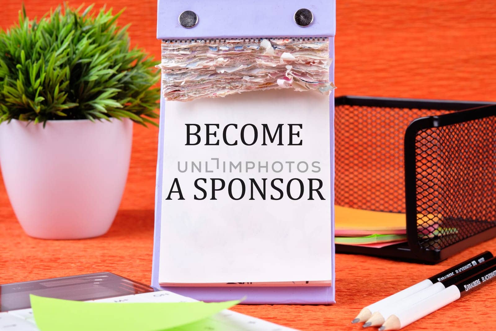 BECOME A SPONSOR text written on the page of the desktop calendar on an orange background