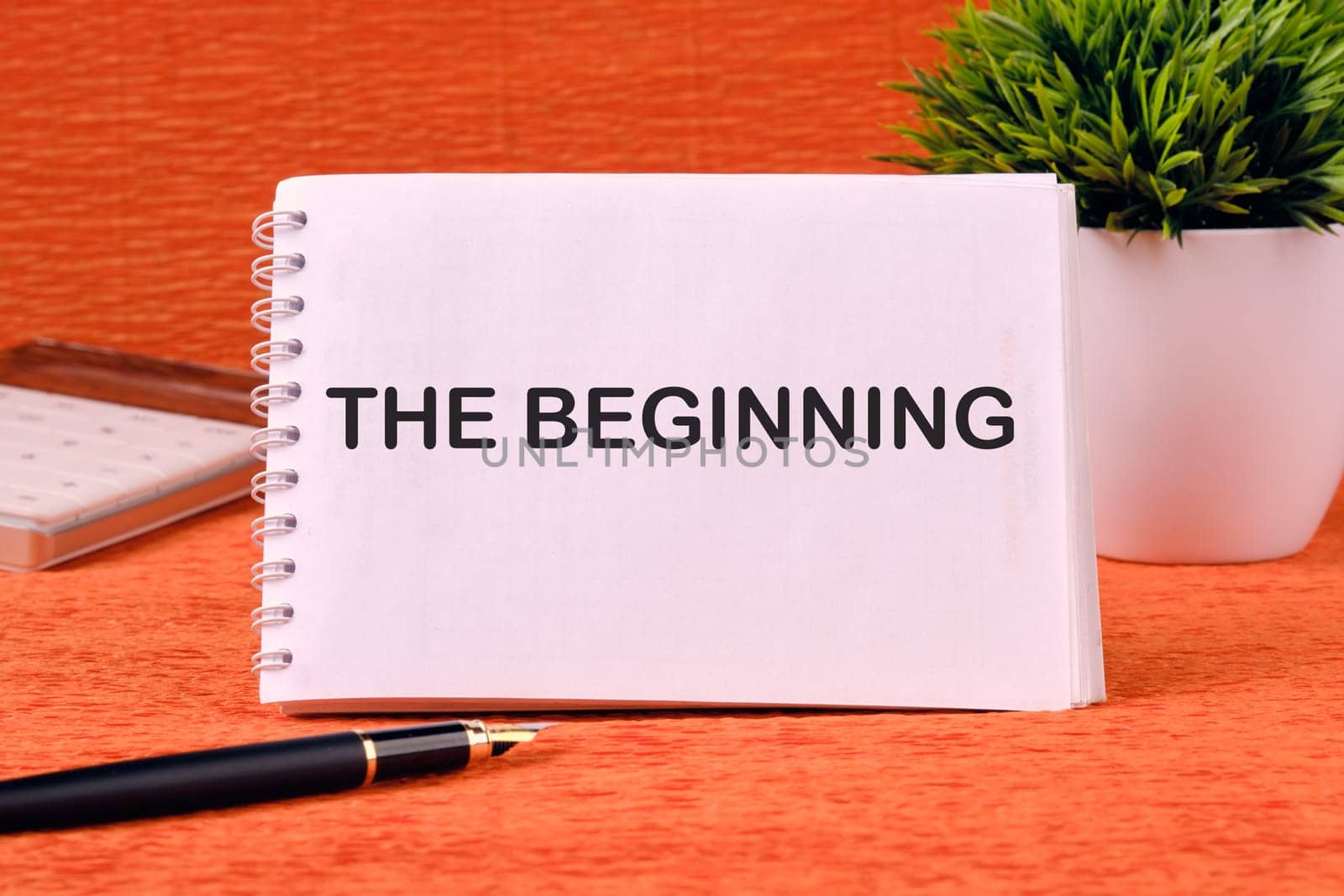 The beginning text written on a blank sheet of notepad, there is a calculator, a pen and a flower in the background