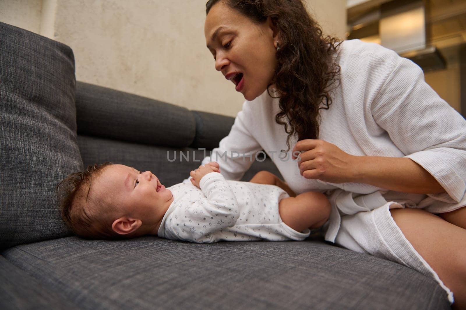 Close-up portrait happy young mother enjoying happy moments with her baby boy during maternity leave, communication,connecting together sitting on a couch at home. Mom and kid face to face, together