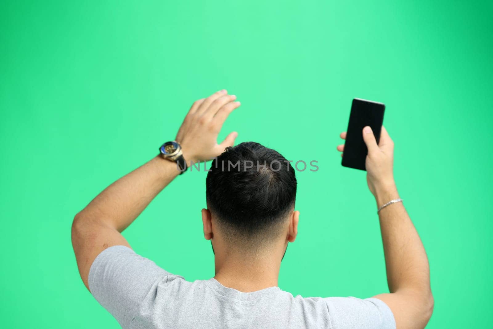 A man, close-up, on a green background, waving his phone.