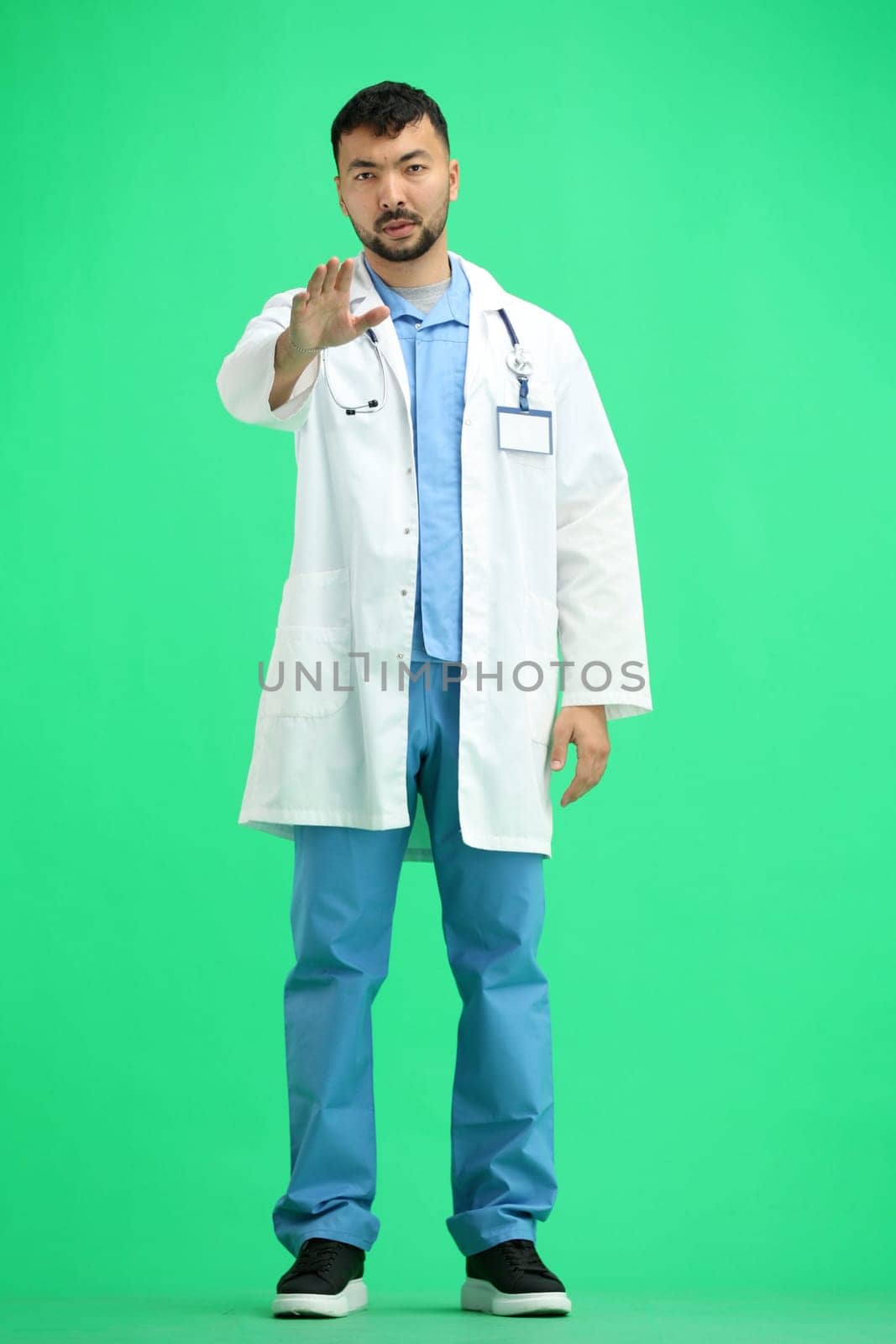 The doctor, in full height, on a green background, shows a stop sign.