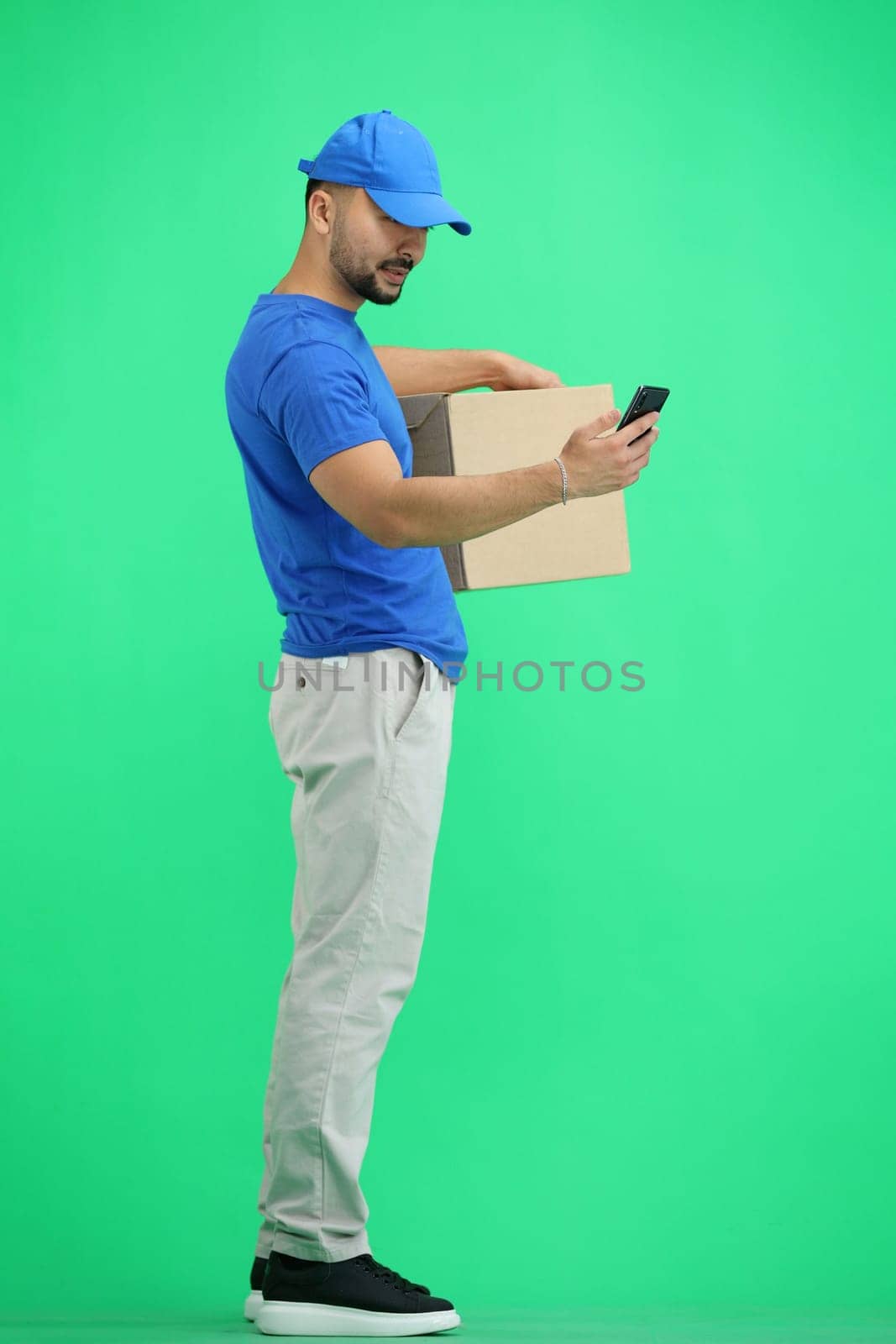 The deliveryman, in full height, on a green background, with a box and a phone.