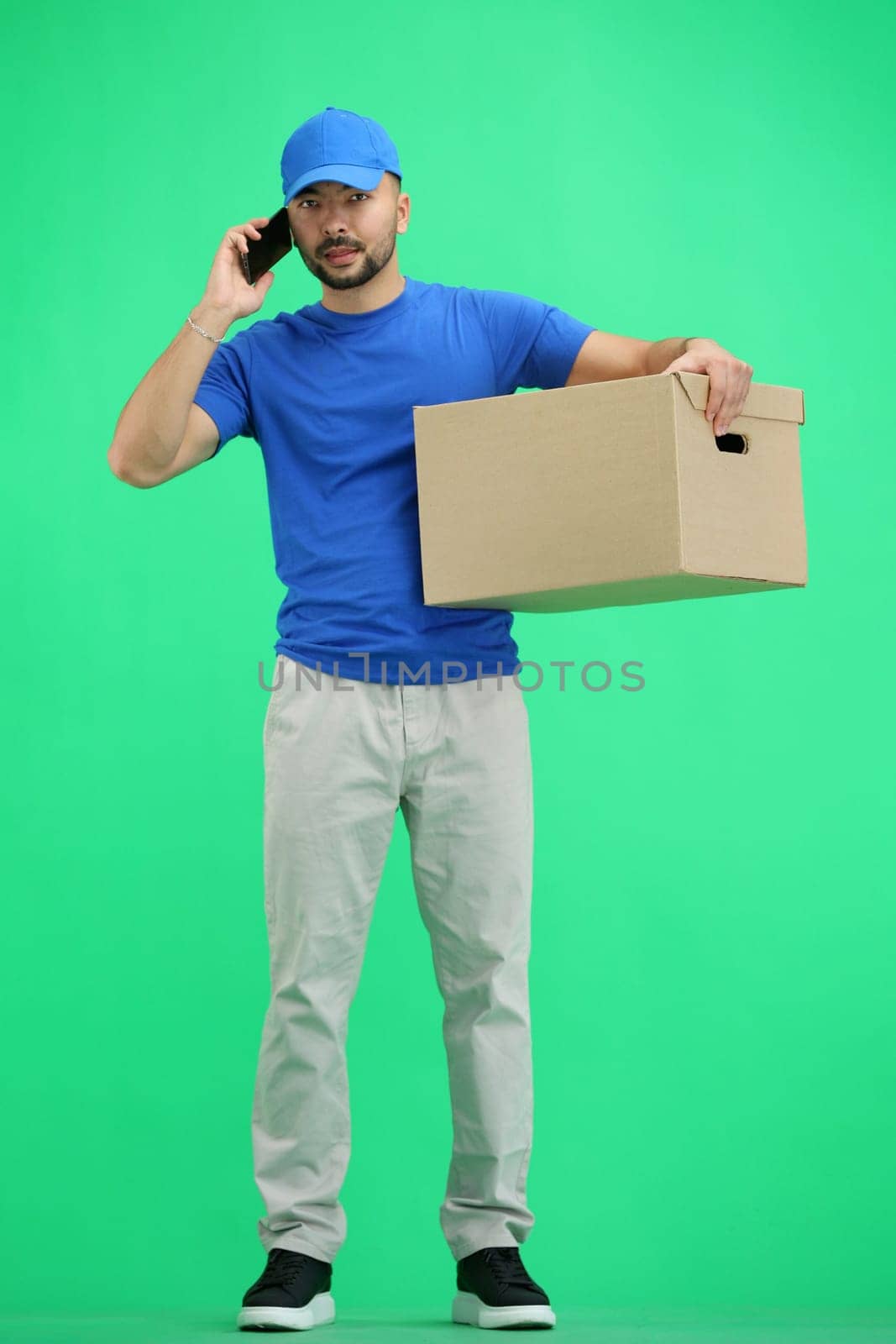 The deliveryman, in full height, on a green background, with a box and a phone.