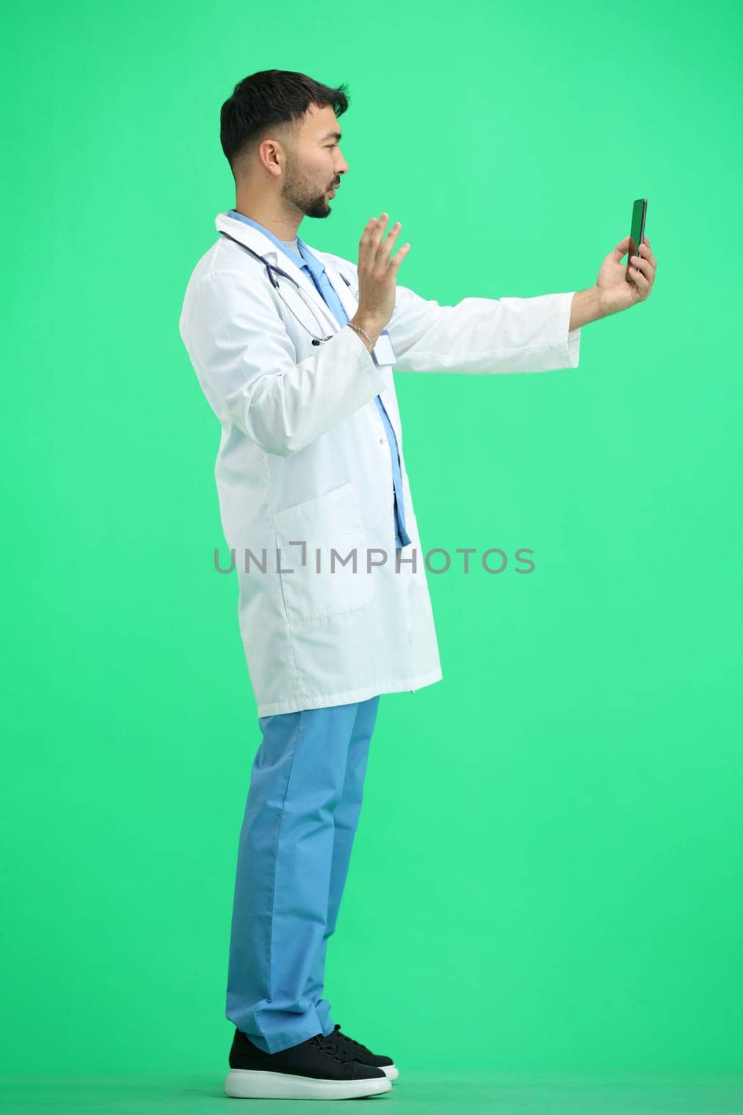 The doctor, in full height, on a green background, talking on the phone.